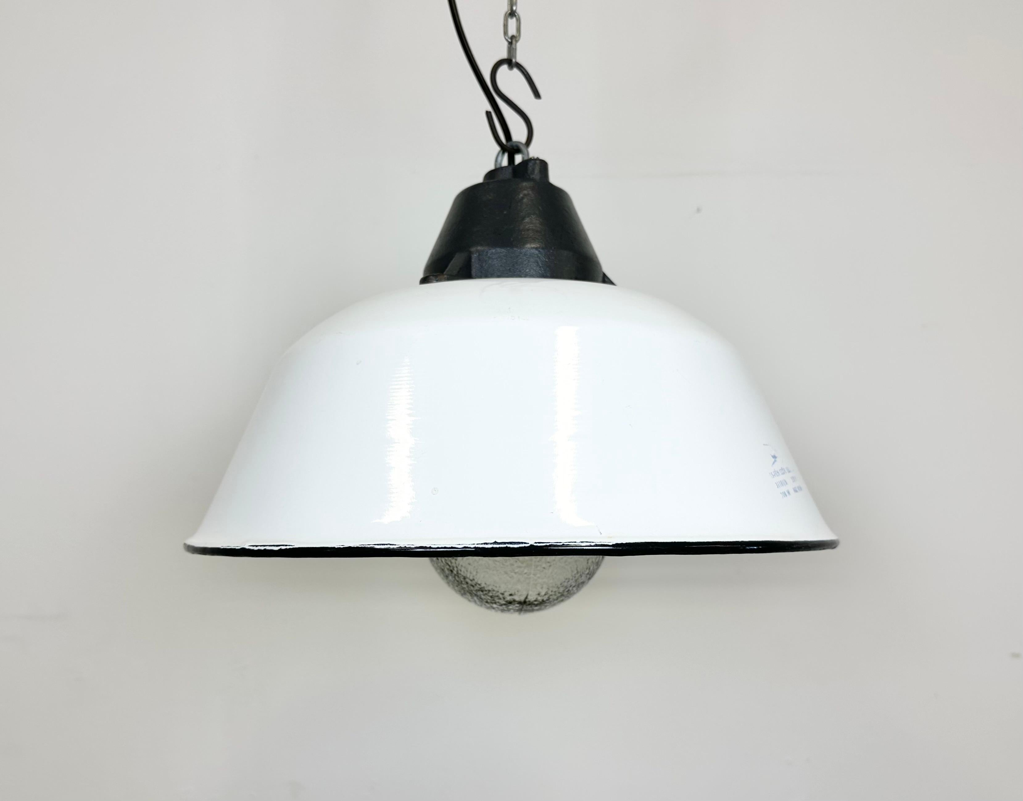 Lampada a sospensione industriale prodotta da Szarvasi Vas - Fém in Ungheria negli anni Sessanta. Presenta un paralume in smalto bianco, un interno in smalto bianco, una parte superiore in ghisa grigia e un coperchio in vetro smerigliato La nuova