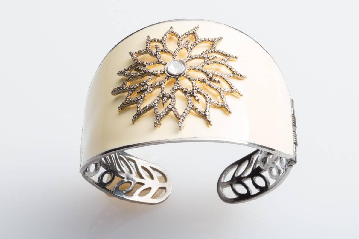 A white enamel, tapered cuff bracelet in oxidized sterling silver with a pave`-set diamond sunburst pattern on the top.  One side is hinged for easy on and off.  Slightly oval with an inside circumference of 6.5 inches.  Carat weight of diamonds is