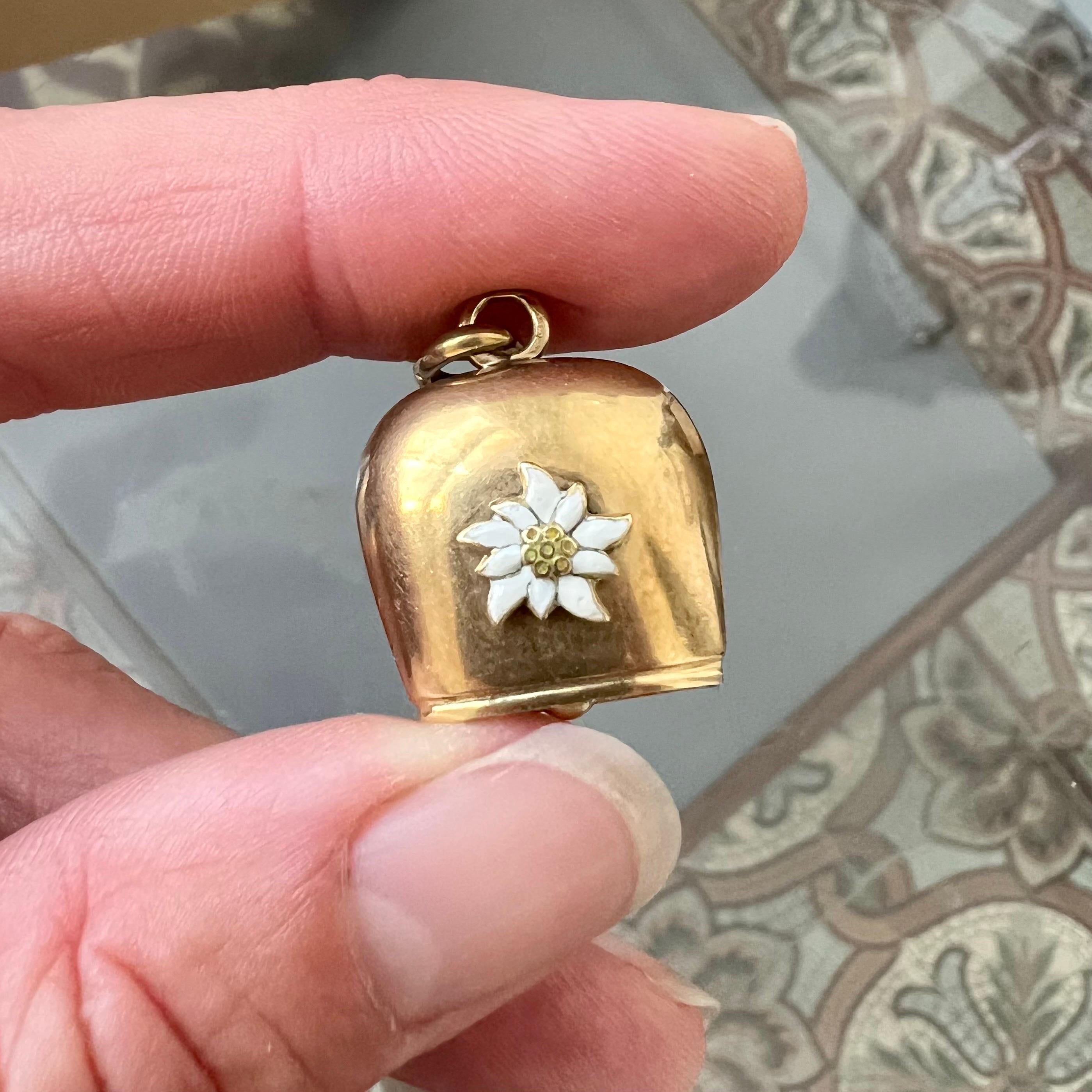 This large vintage 14-karat yellow gold Swiss cow bell charm pendant is a striking and unique piece of jewelry. It features a beautifully crafted white enameled edelweiss flower set prominently on the front of the bell, adding a touch of elegance