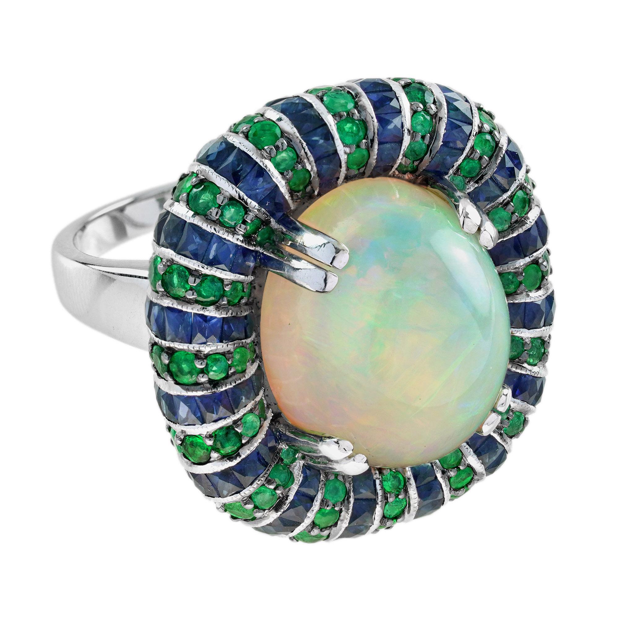 A delightful antique style ring is centered with one prong set, vibrant 11.7 carat oval cabochon cut natural Ethiopian opal. The opal is bordered with 144 French cut blue sapphires and 133 round emerald all set in 18k white gold. This ring is