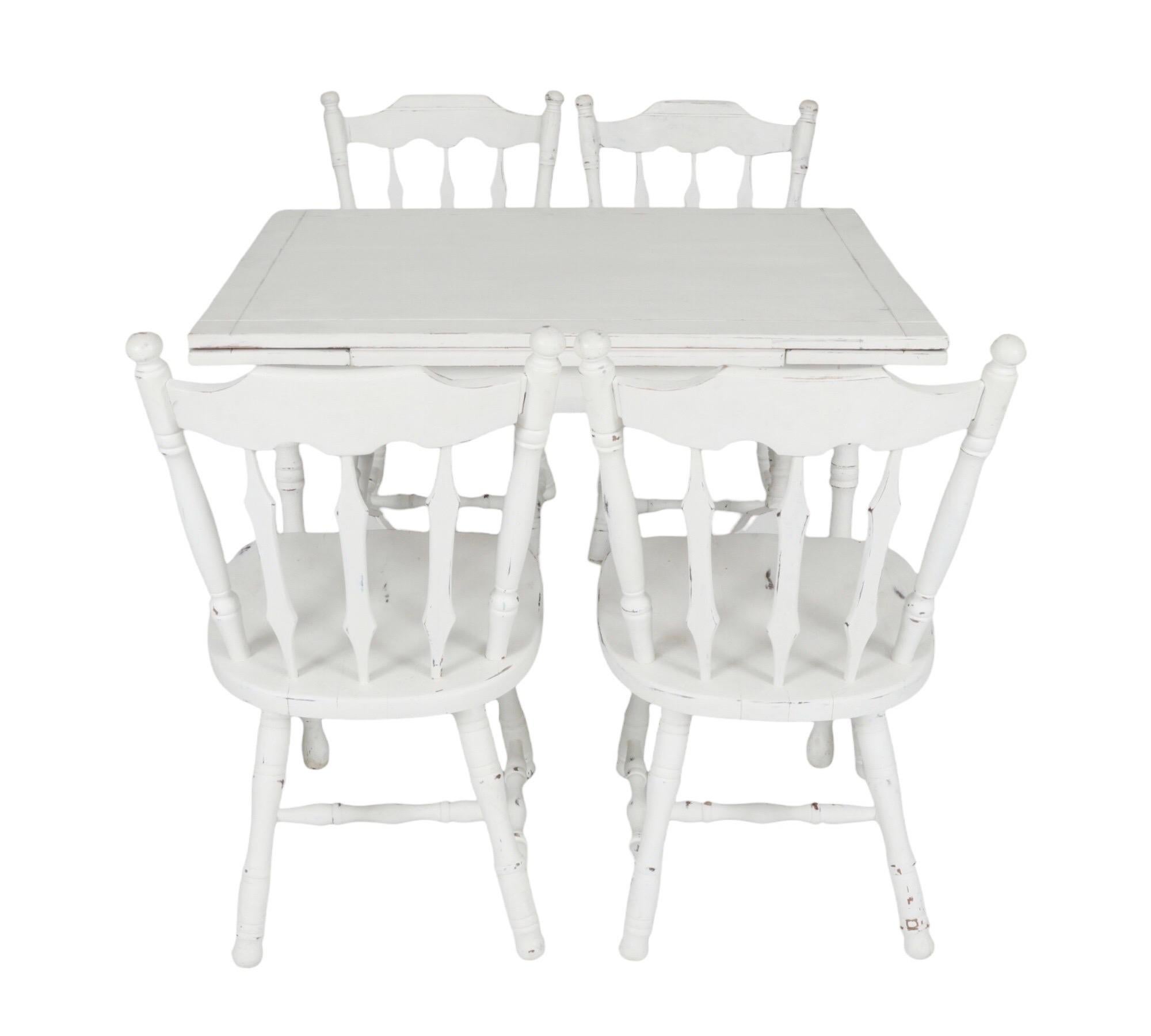 A white farmhouse kitchen table with four matching dining chairs. The table extends with two pull out leaves to seat six. The table is decorated with a carved line border and stands on turned legs secured with an ‘x’ stretcher. Four side chairs have