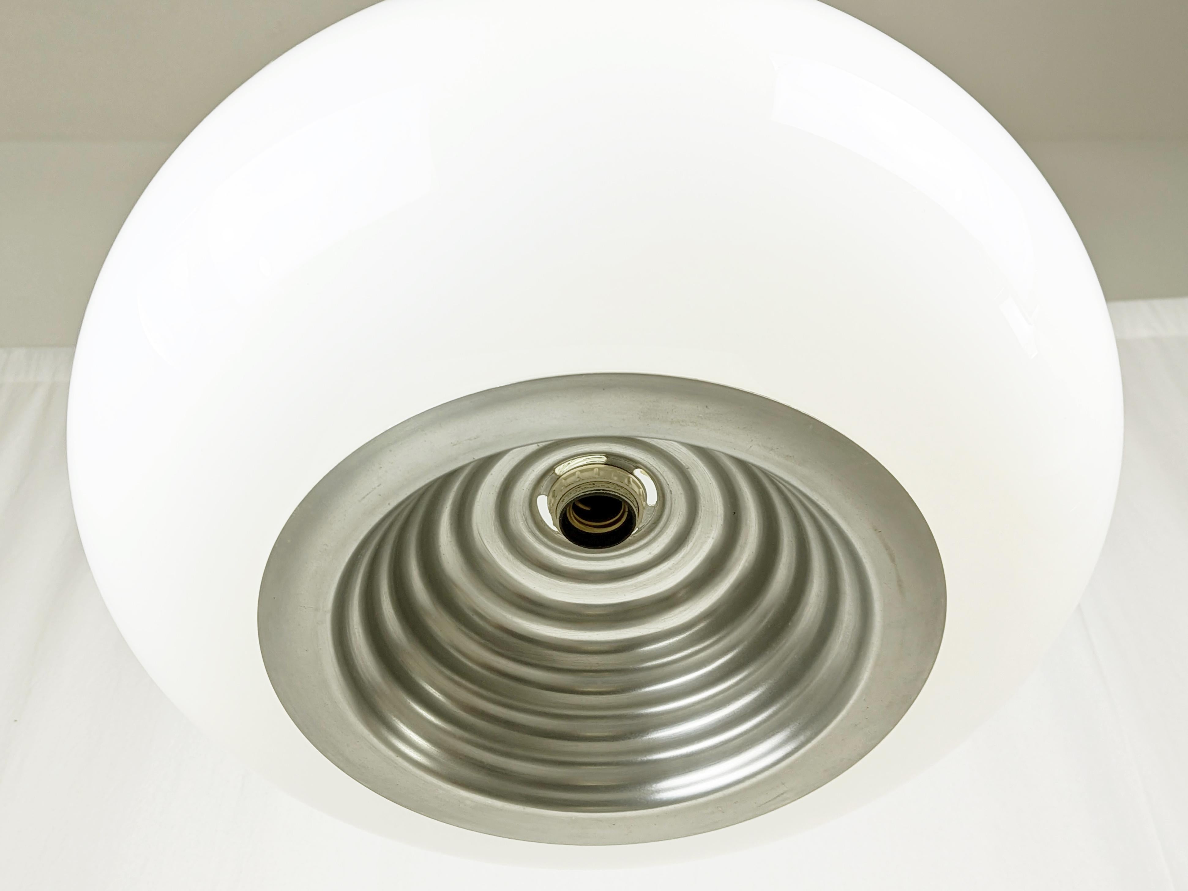This out of production pendant was made from a white opaline glass shade with a shaped silver aluminum reflector. The lamp features 2 different illuminations: one diffused light from the 3 bulbs inside the glass shade; and one directed light from