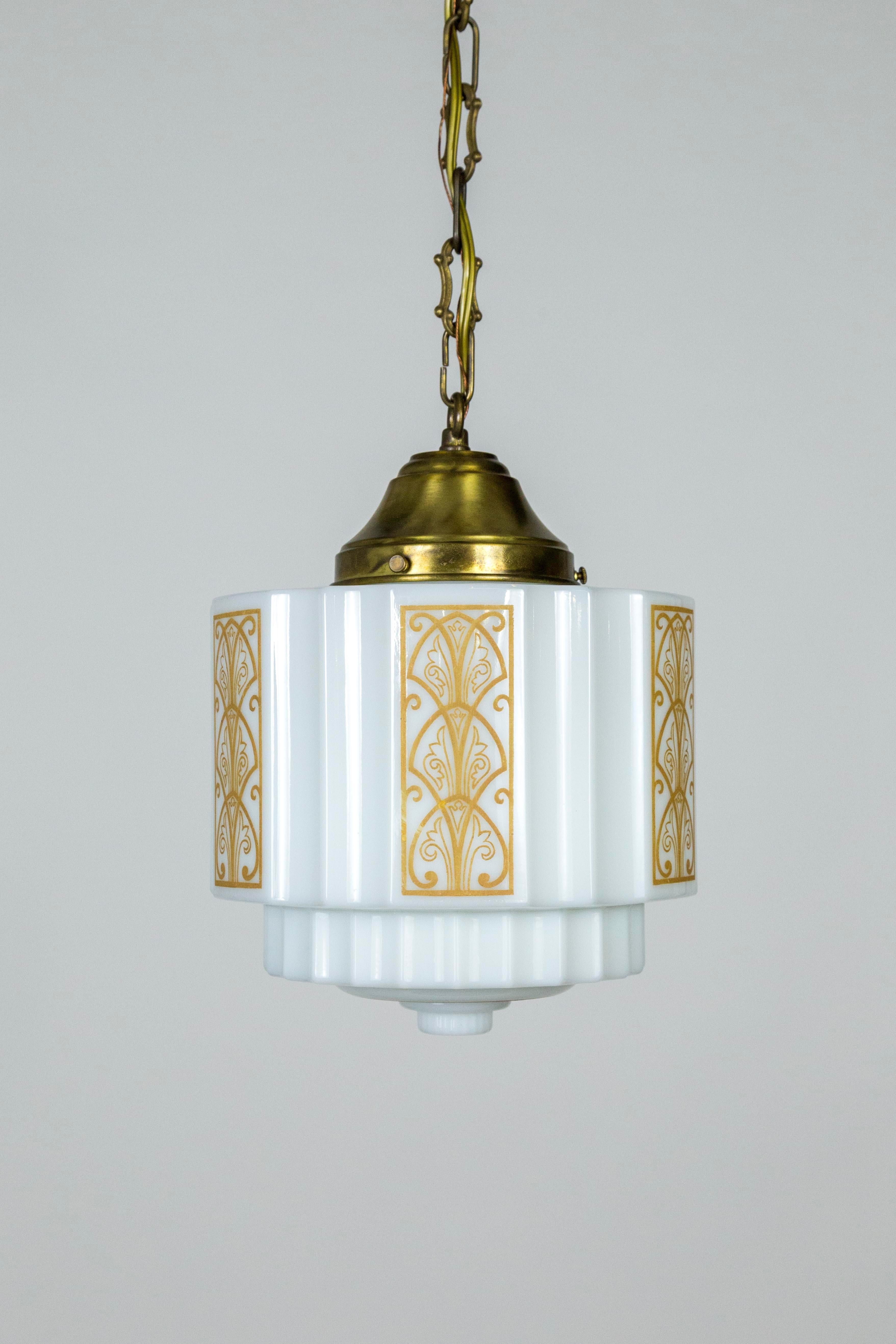 An Art Deco pendant with ridged, molded white glass in a stepped, cylinder shape, painted with sienna colored decorations; with a decorative, brass chain and lovely, copper toned canopy, 1920s. Measures: 8
