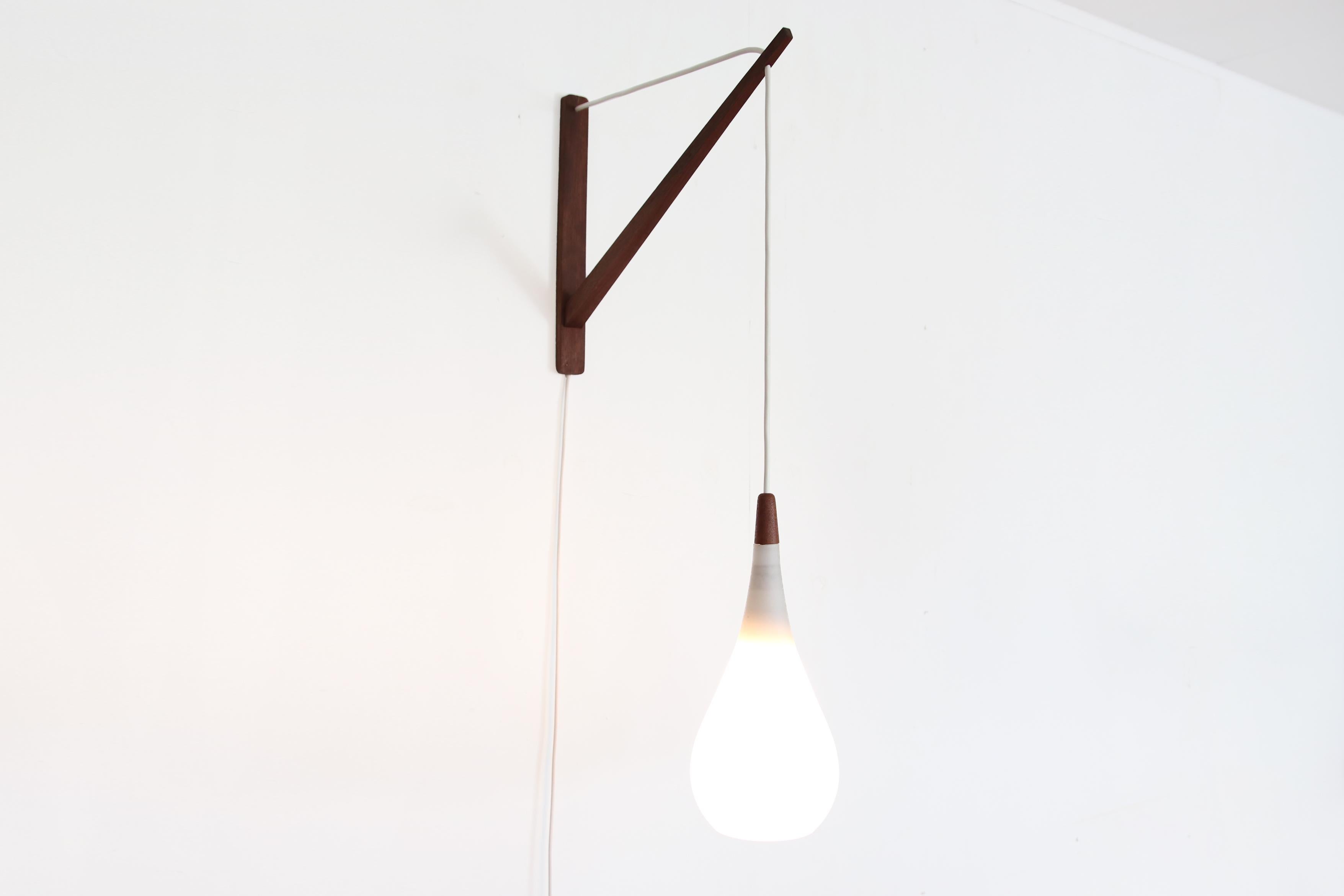 Very beautiful and sophisticated wall lamp from the Danish manufacturer Holmegaard. The opal white glass in teardrop shape with teak detail hangs from a minimalist teak wall fixture. The lamp is marked 