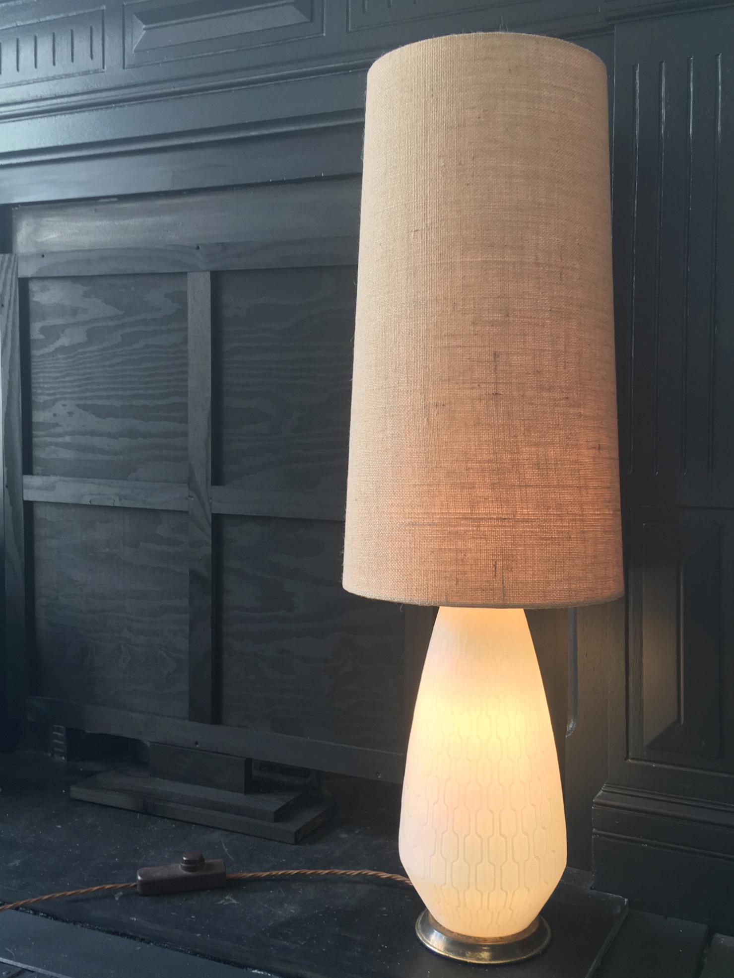 White glass Mid-Century Modern table or floor lamp with brass base and three-way switch, European. 

The lamp base is made of white satin glass with a raised geometric pattern, and is fitted with a three-way switch allowing light to come through the