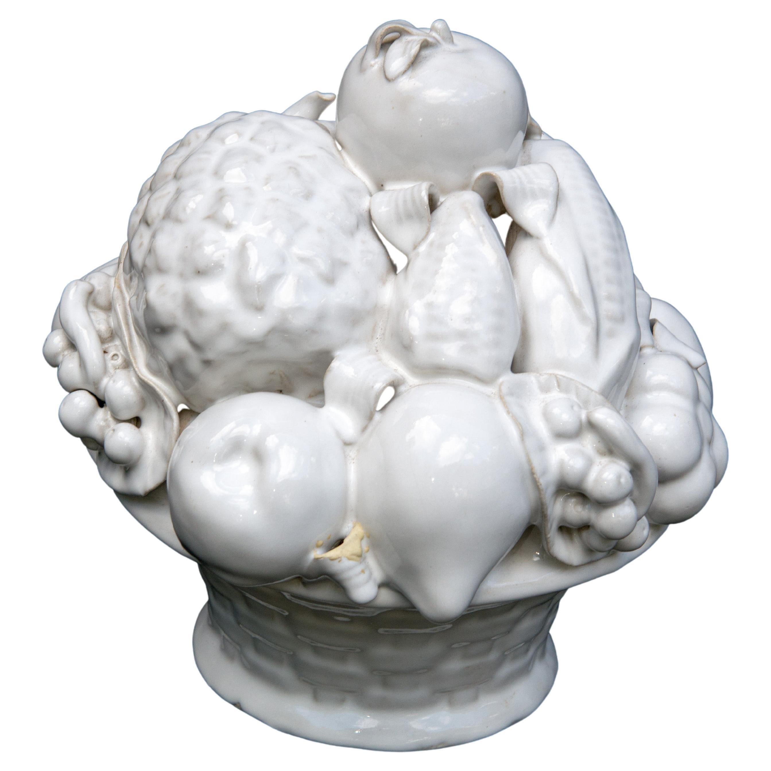 A white glazed ceramic basket of fruit, probably Italian. The pineapple stem has been repaired with a small loss. The leaf of another fruit has two two areas of mismatched filling. A stunning piece nevertheless.