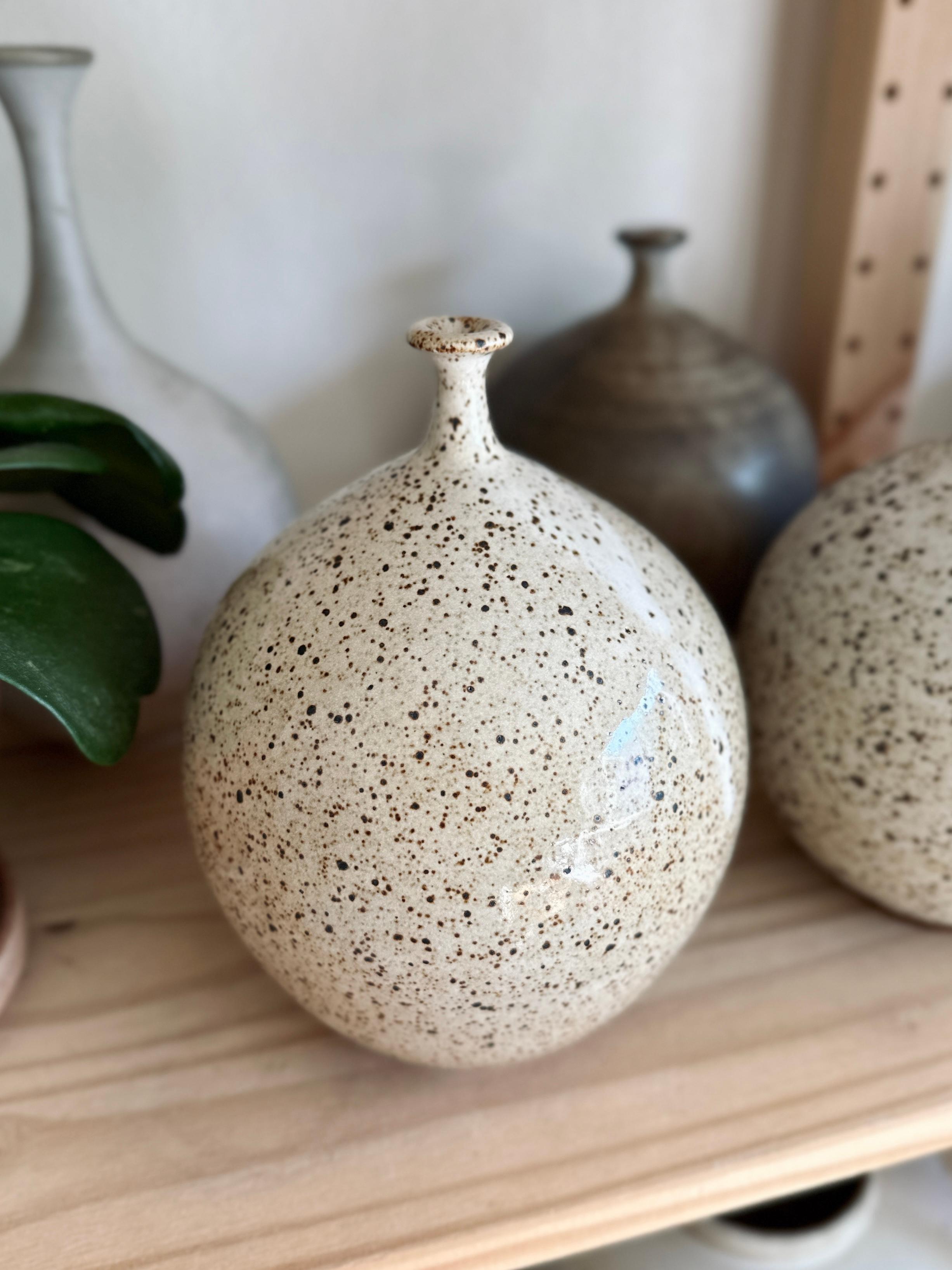 Wheel-thrown speckled bottleneck vessel glazed in warm glossy white. Handmade from stoneware, this piece serves as a testament to the timeless beauty of heirloom pottery, bringing an organic serenity to your dearest spaces. 

Dimensions: 7.5”t x