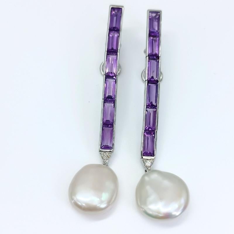Long earrings in white gold with omega clasp.
12 baguette-cut amethysts, 2 brilliant-cut diamonds and two coin pearls.

18k White Gold
12 Amethysts 16.50k
2 Diamonds 0.16k
2 Coin Pearls