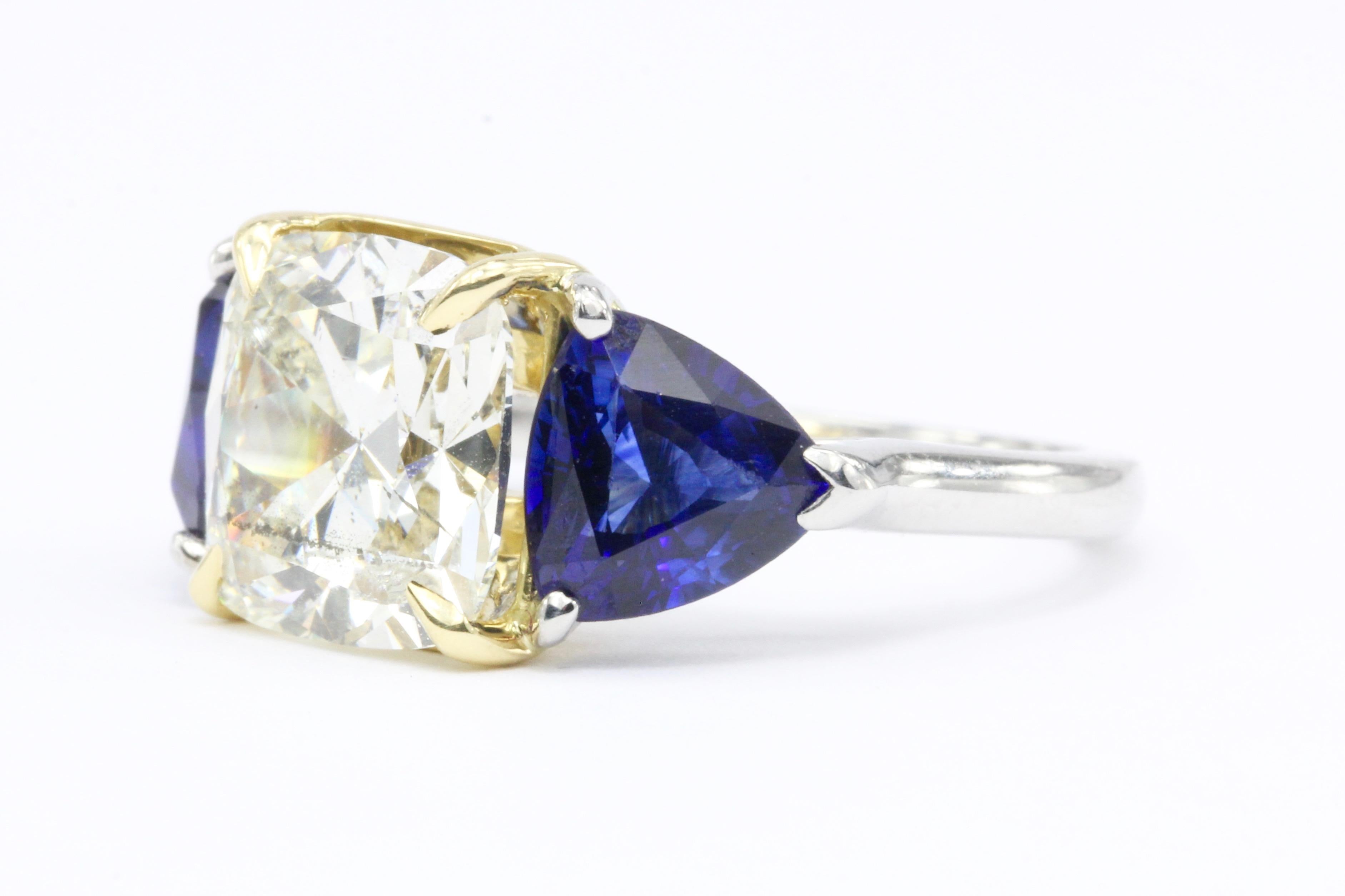 Hallmarks: PT 950 750

Composition: 18K White Gold & Platinum Setting

Primary Stone: Cushion Cut Diamond

Stone Carat: 3.11 Carats

Color / Clarity: M / I1

Accent Stone: 2 .75 carats (1.5 ctw) Trillion Cut Natural Blue Sapphires

Ring Width: