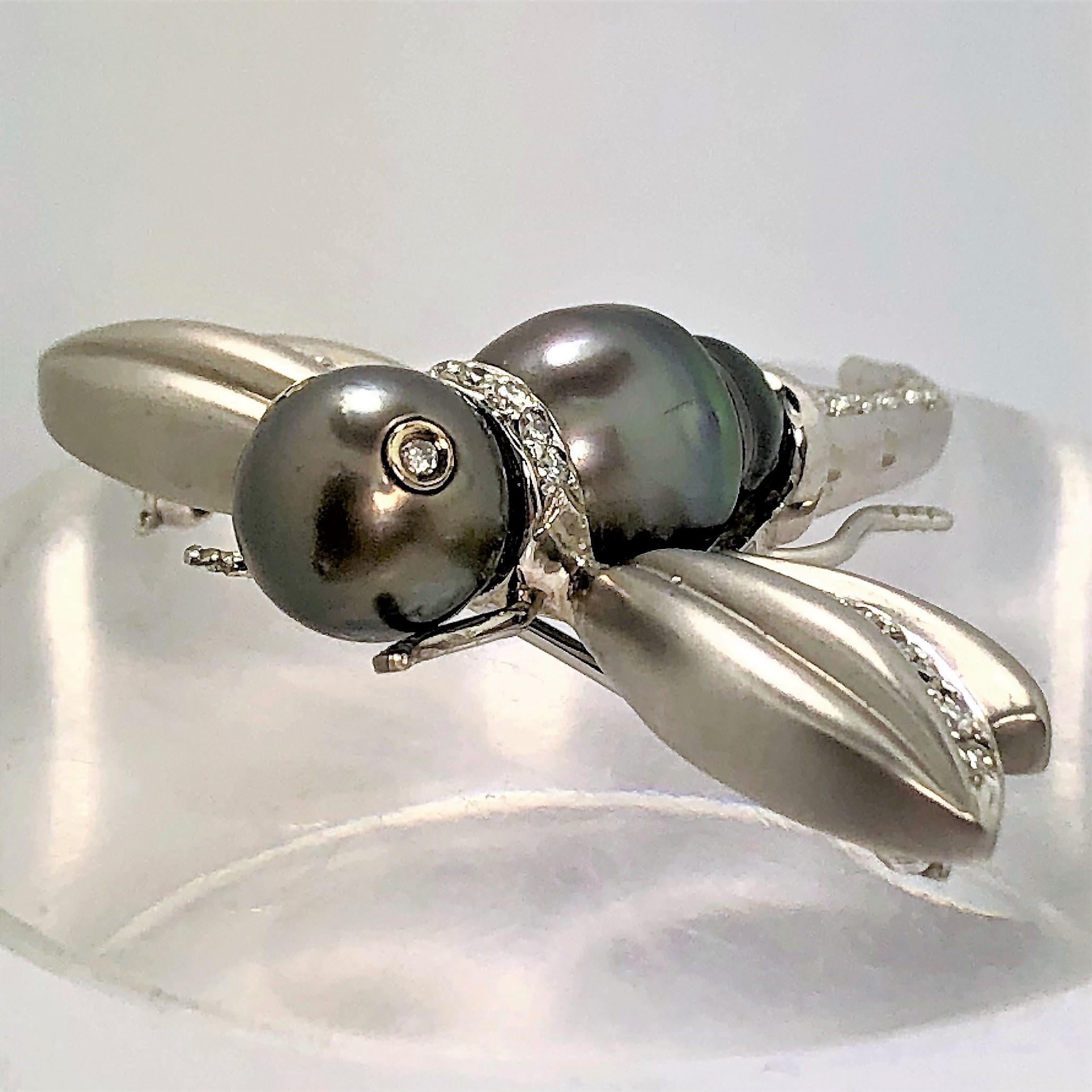 This adorable, satin finish, 18K white gold flying insect brooch has an 8.75mm black pearl 
head with two diamond eyes and a black semi-baroque pearl body, accented with 32 
round brilliant cut diamonds. 
In addition to the diamond eyes, it has a
