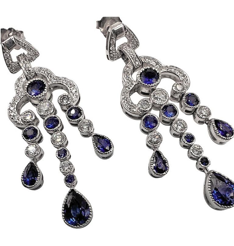 Blue sapphire and diamond chandelier earrings in polished 14k white gold.  Delicate milgrain edge border accents the arch design.  Three tassel-style drop sections move like chandelier pendants and are set with round brilliant-cut diamonds weighing