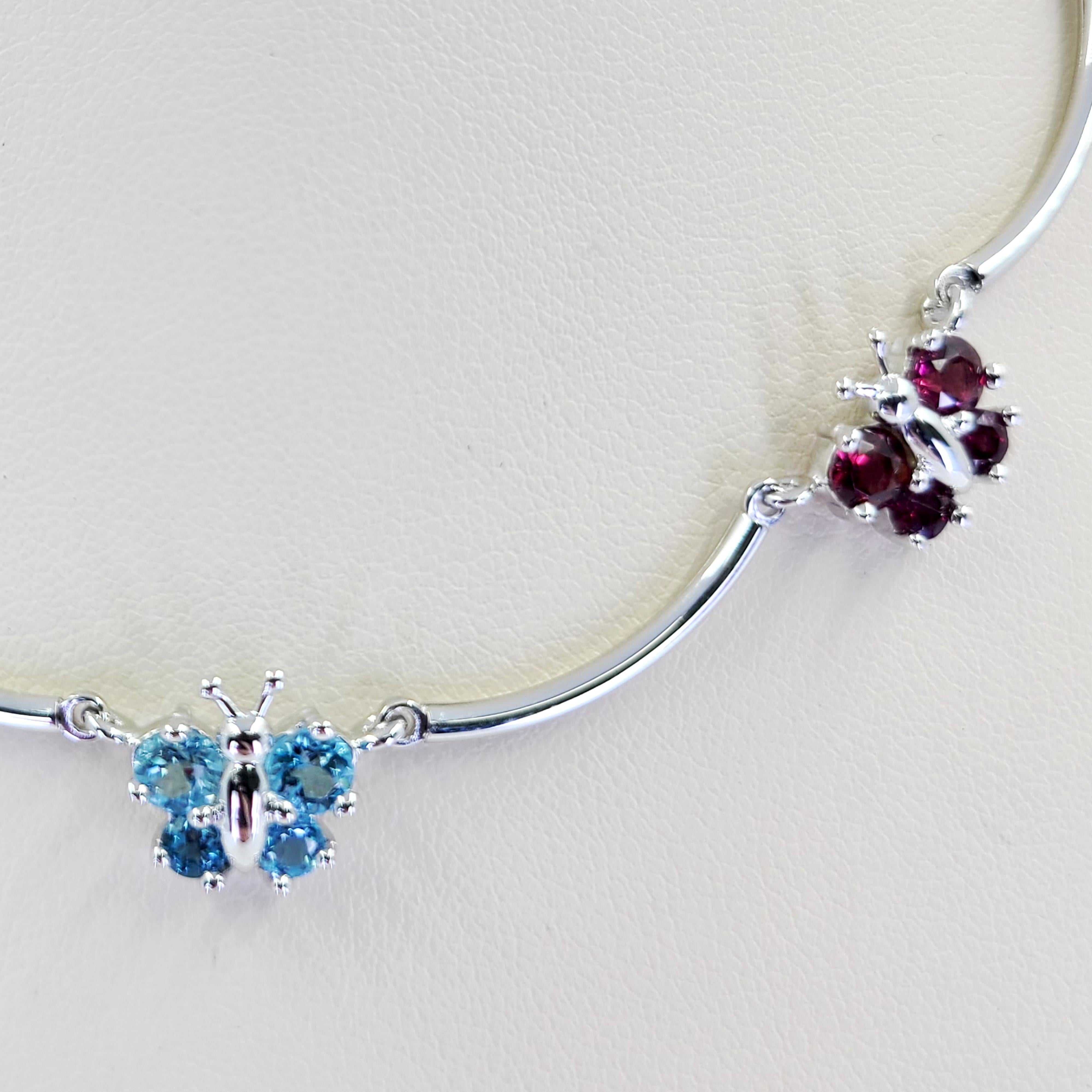 18 Karat White Gold Scalloped Butterfly Collar Necklace Featuring 12 Round Blue Topaz Totaling Approximately 1.00 Carat and 8 Round Garnet Totaling Approximately 0.60 Carat. 15 Inch Length with Lobster Clasp. Finished Weight Is 15.0 Grams.