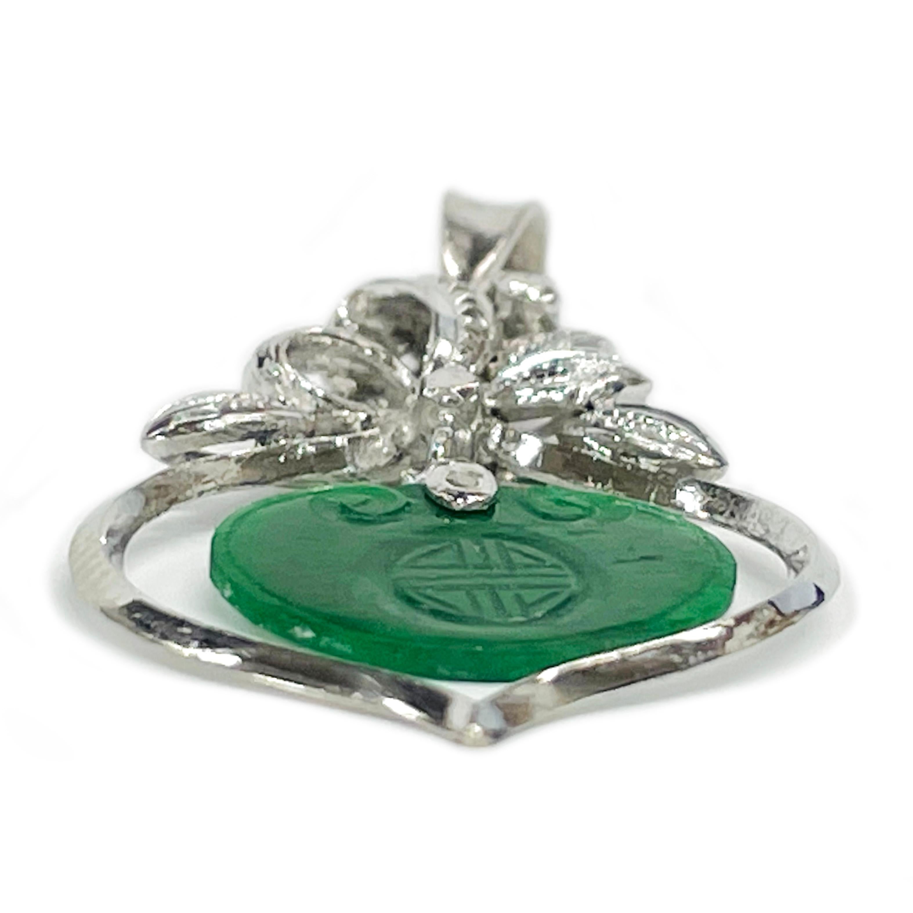 18 Karat White Gold Carved Jade Chinese Pendant. This lovely and petite pendant features a floral ribbon-like detail with an open teardrop shape and a dangling green jade piece. The jade piece has two delicately carved scrolls and a Chinese symbol.