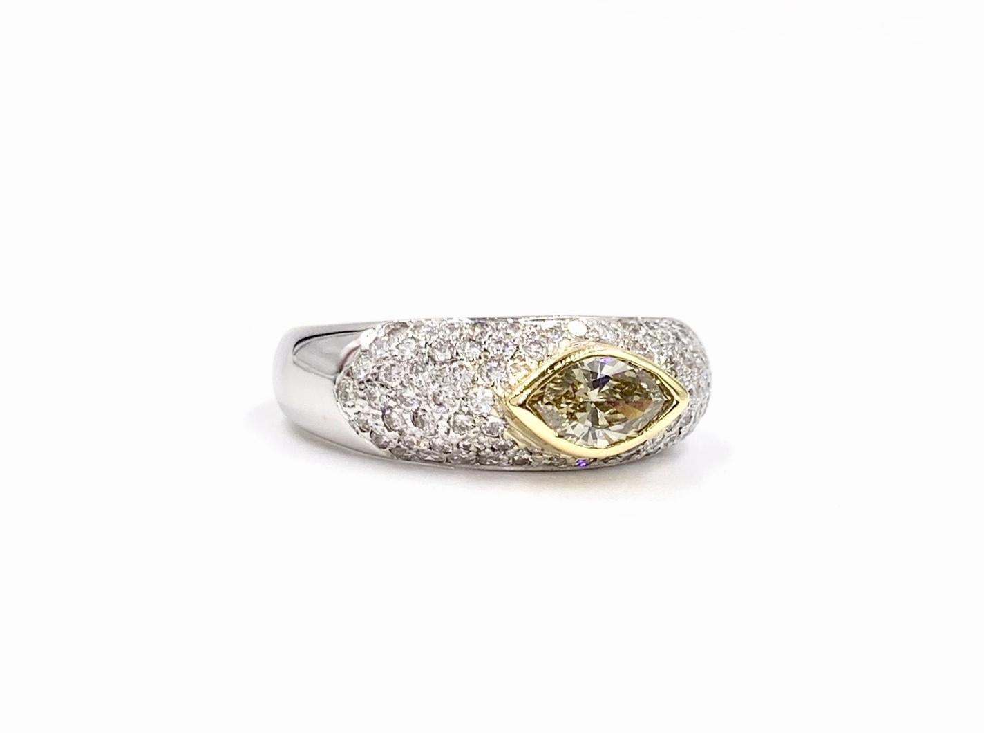 A wearable and comfortable 14 karat white gold slightly domed ring featuring a champagne color marquise center diamond, showing it's warmth as it is beautifully bezel set in yellow gold surrounded by pavé set white diamonds. Marquise has an