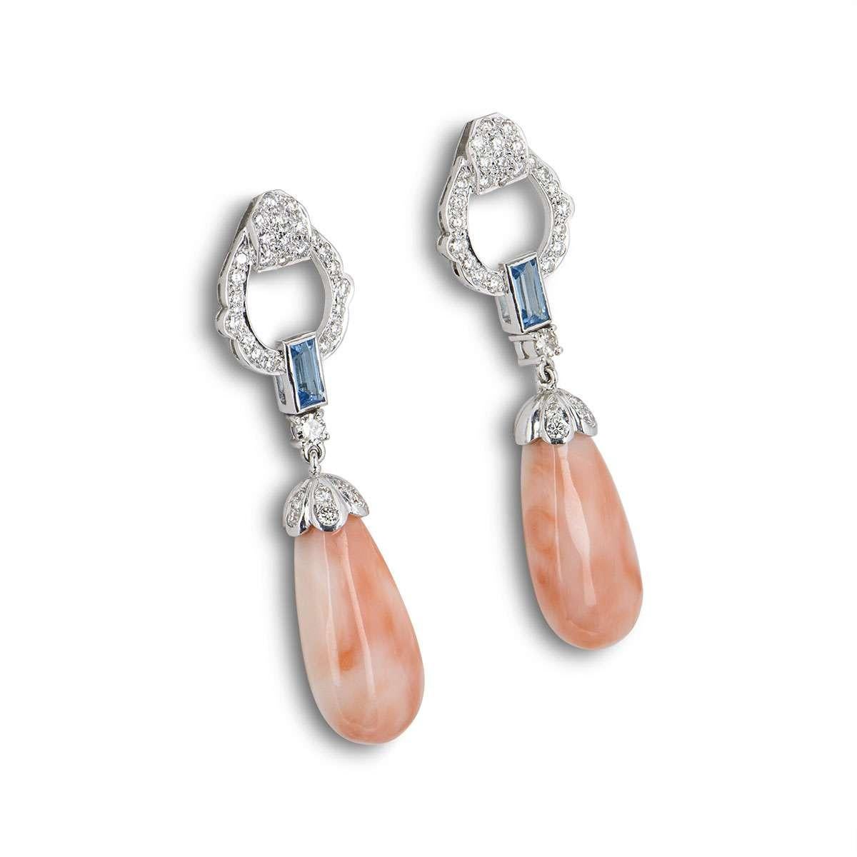 A lovely pair of 18k white gold drop earrings. The earrings feature pave set round brilliant cut diamonds with a single baguette cut blue topaz, suspending a large piece of coral in a teardrop shape. The diamonds have a total weight of 1.71ct, the