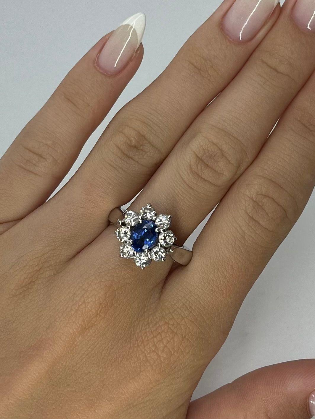 Questo squisito anello a margherita è realizzato in oro bianco 18 carati (750/1000) e mette in mostra uno splendido zaffiro di Ceylon da 1,62 carati dalla vibrante tonalità blu, probabilmente non trattato, che aggiunge rarità e bellezza naturale. Lo