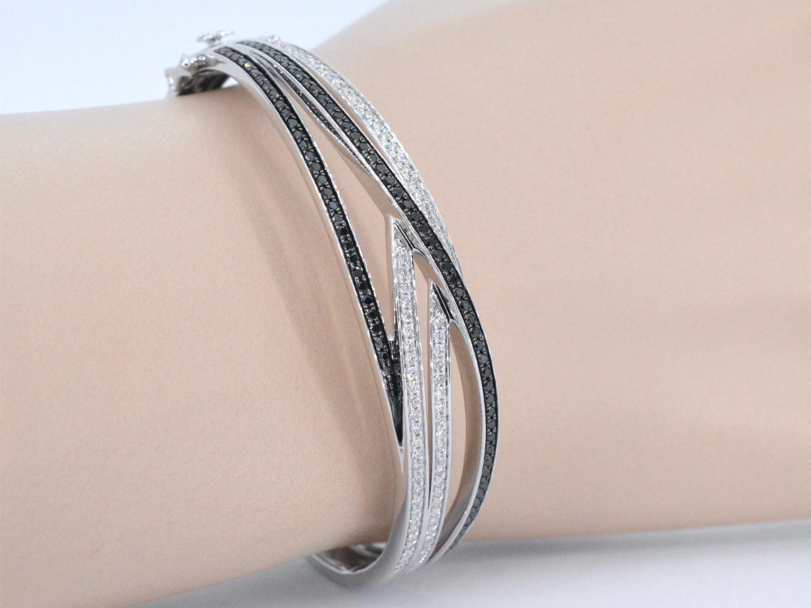 This white gold bracelet is a unique and stylish piece of jewelry that features a stunning design with white and black brilliant diamonds. The diamonds are expertly arranged in a pattern that creates a beautiful contrast between the white and black