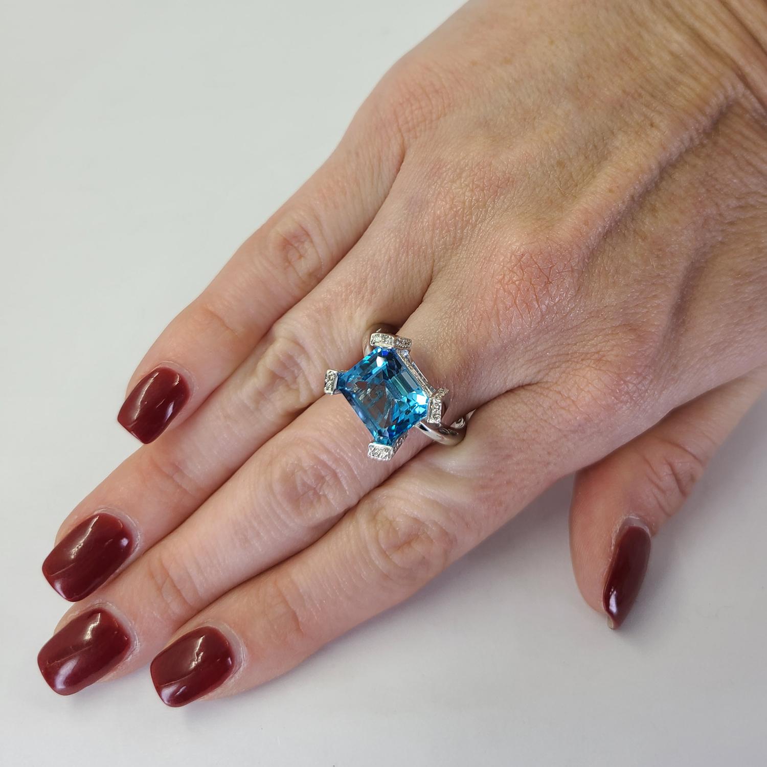 18 Karat White Gold Ring Featuring An Emerald Cut Blue Topaz Weighing Approximately 5 Carats Accented By 58 Round Diamonds Of VS Clarity & H Color Totaling 0.58 Carats. Finger Size 8.5. Finished Weight Is 8.6 Grams.