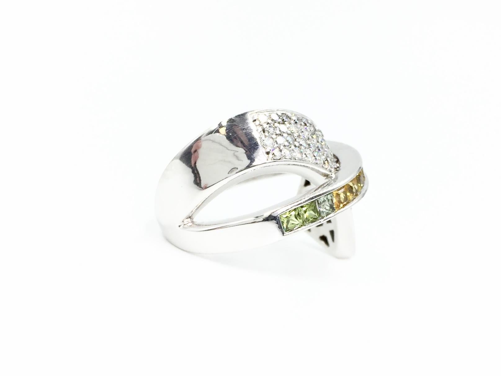 Dramatic, vivid and fun cross over ring made in 14 karat white gold and featuring pavé white diamonds and a range of colorful princess cut sapphires. Light green, yellow, pink, periwinkle and blue sapphires are securely set in a channel crossing