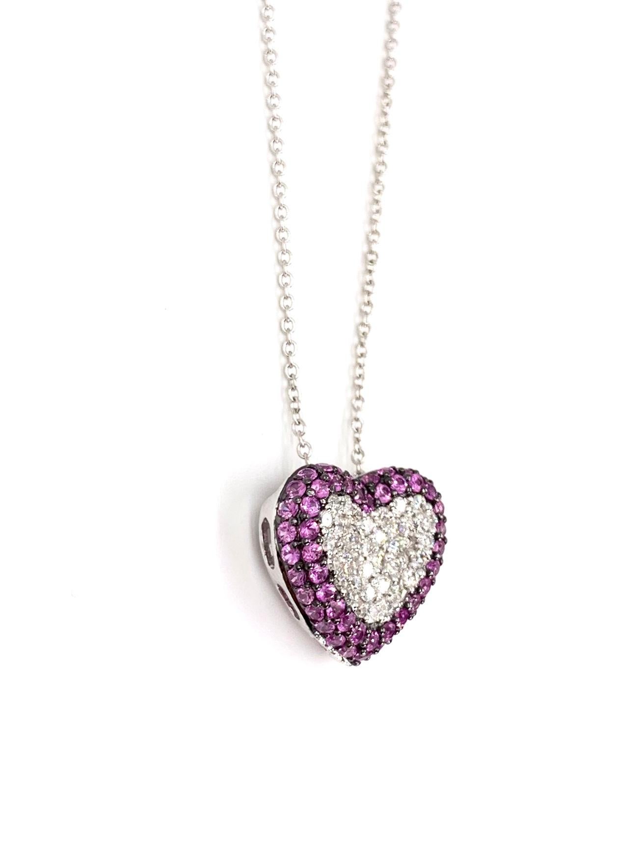 A 14 karat white gold puffed heart slide pendant is adorned with expertly pavé set round brilliant white diamond and vivid pink sapphires. Approximate diamond total weight is .50 carat at approximately G color, VS2 clarity surrounded by two rows of