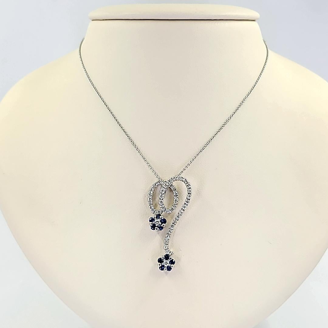 Whimsical and Feminine 18 Karat White Gold Drop Flower Pendant Featuring 10 Round Sapphires Totaling 0.50 Carats and 40 Round Diamonds of SI Clarity and H/I Color Totaling 0.25 Carats. 1.5 Inches Long. Finished Weight Is 3.9 Grams. Chain Sold