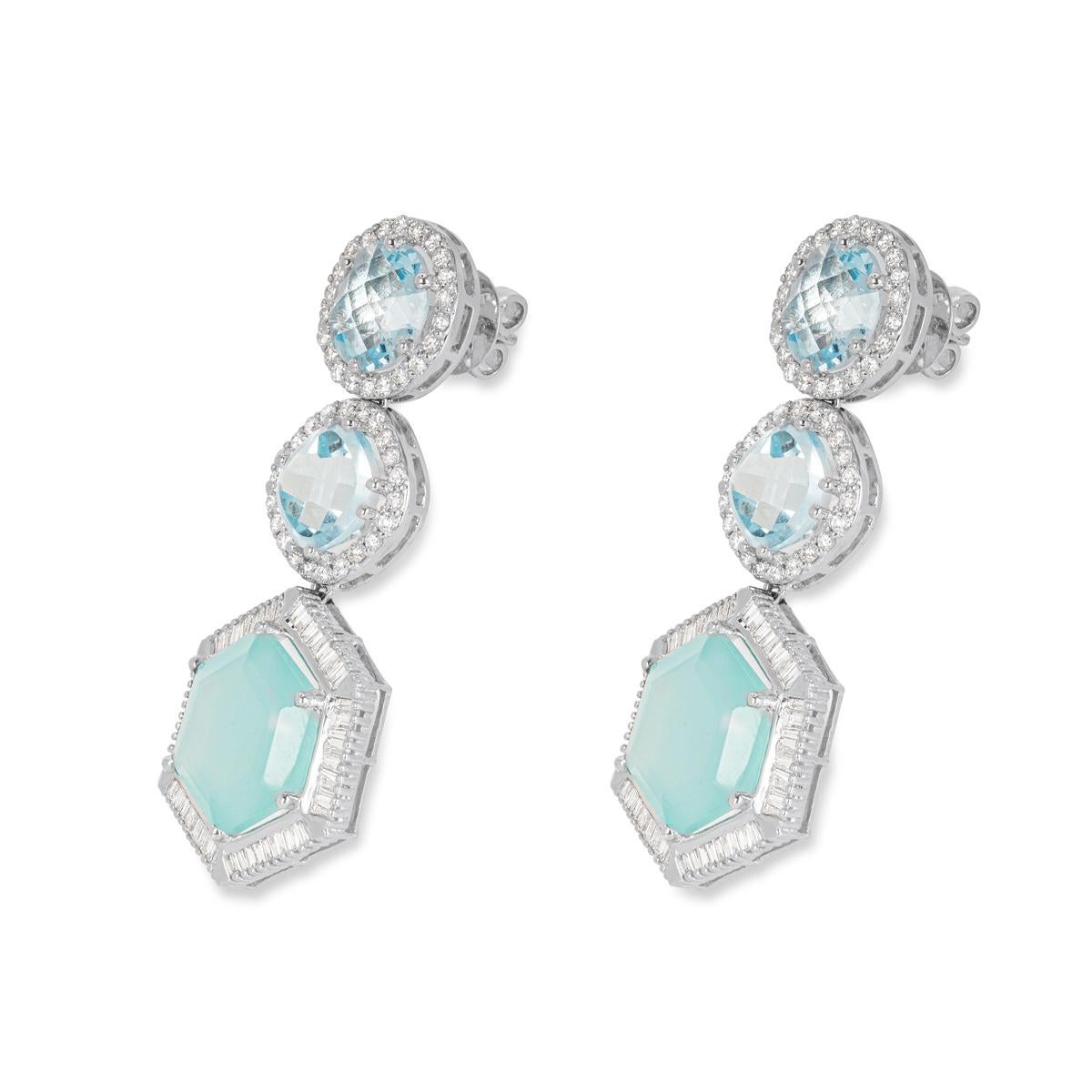 A unique pair of 14k white gold diamond and topaz drop earrings. The earrings each comprises of a round cut, cushion cut and a multi-faceted topaz vertically placed with a halo of diamonds around each. The topaz has a total weight of 35.30ct with a
