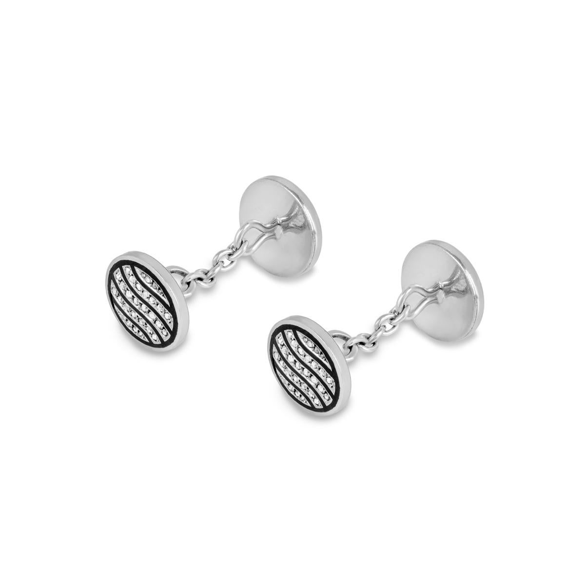 A pair of 18k white gold diamond and enamel inlay cufflinks. The cufflinks are composed of a circular motif featuring a black enamel inlay, each pave set with 30 free form diamonds set within four intersections. The cufflinks are completed with a