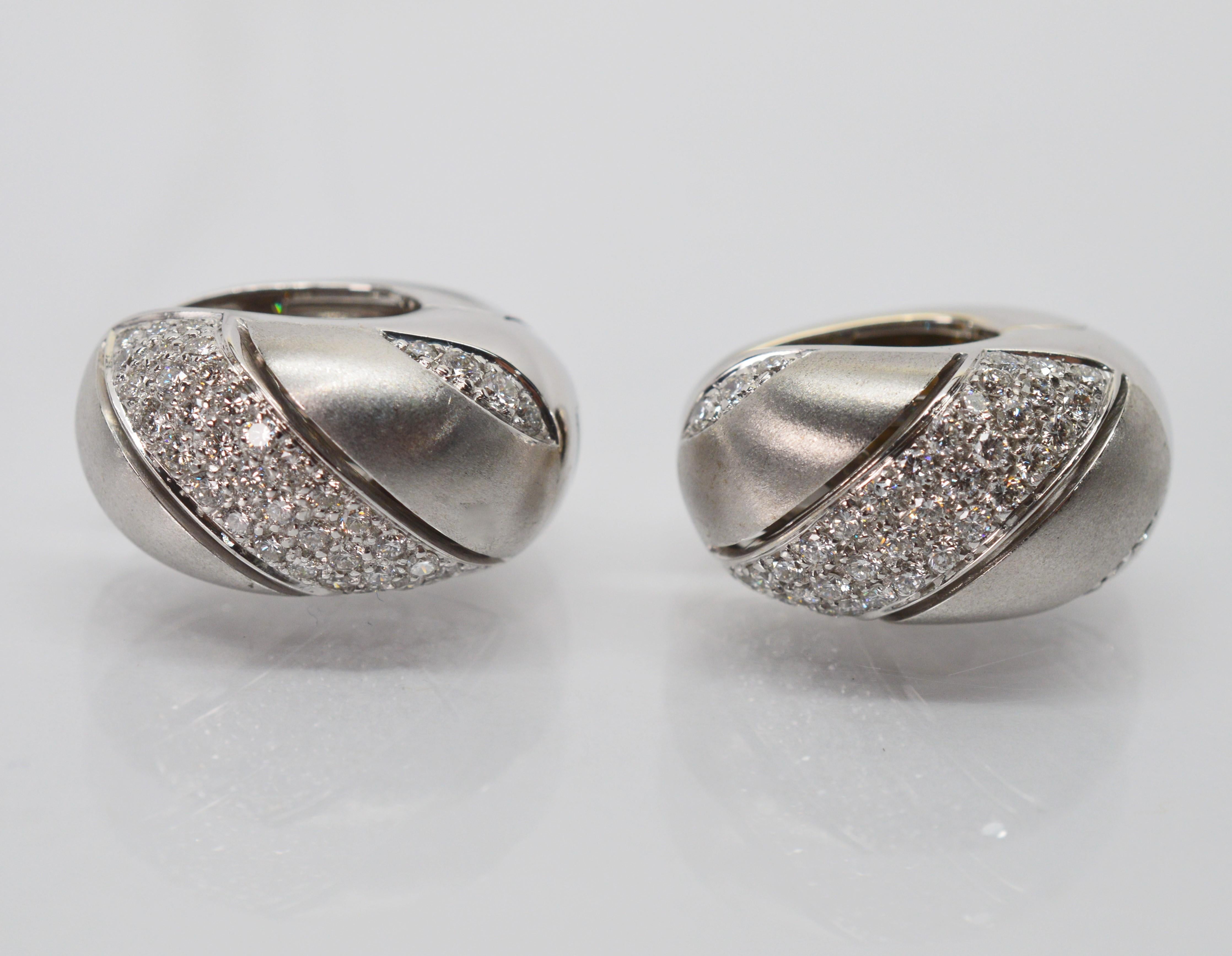 A ribbon of diamonds flashes across the satin finished eighteen karat (18K) white gold of these quality Italian made huggie hoop style earrings giving them a regal look. Ninety-four H/VS round diamonds weighing almost a carat illuminates this pair