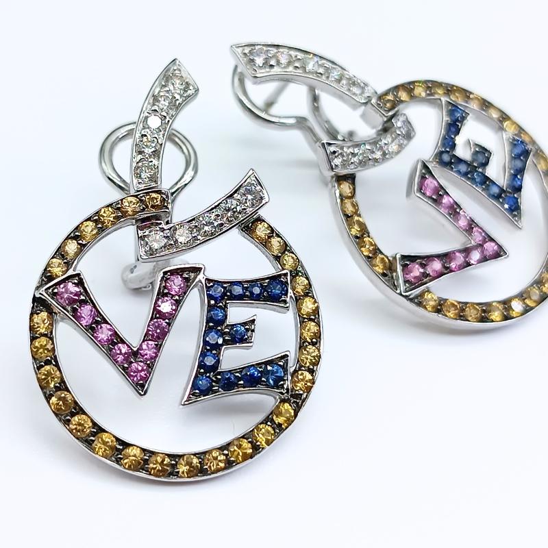 White Gold earrings with the word LOVE with omega clasp. 
20 brilliant cut diamonds, 24 blue Sapphires, 54 yellow Sapphires and 18 pink Sapphires.

18k White Gold
20 Diamonds 0.53k
24 Blue Sapphires 0.48k
54 Yellow Sapphires 1.25k
18 Pink Sapphires