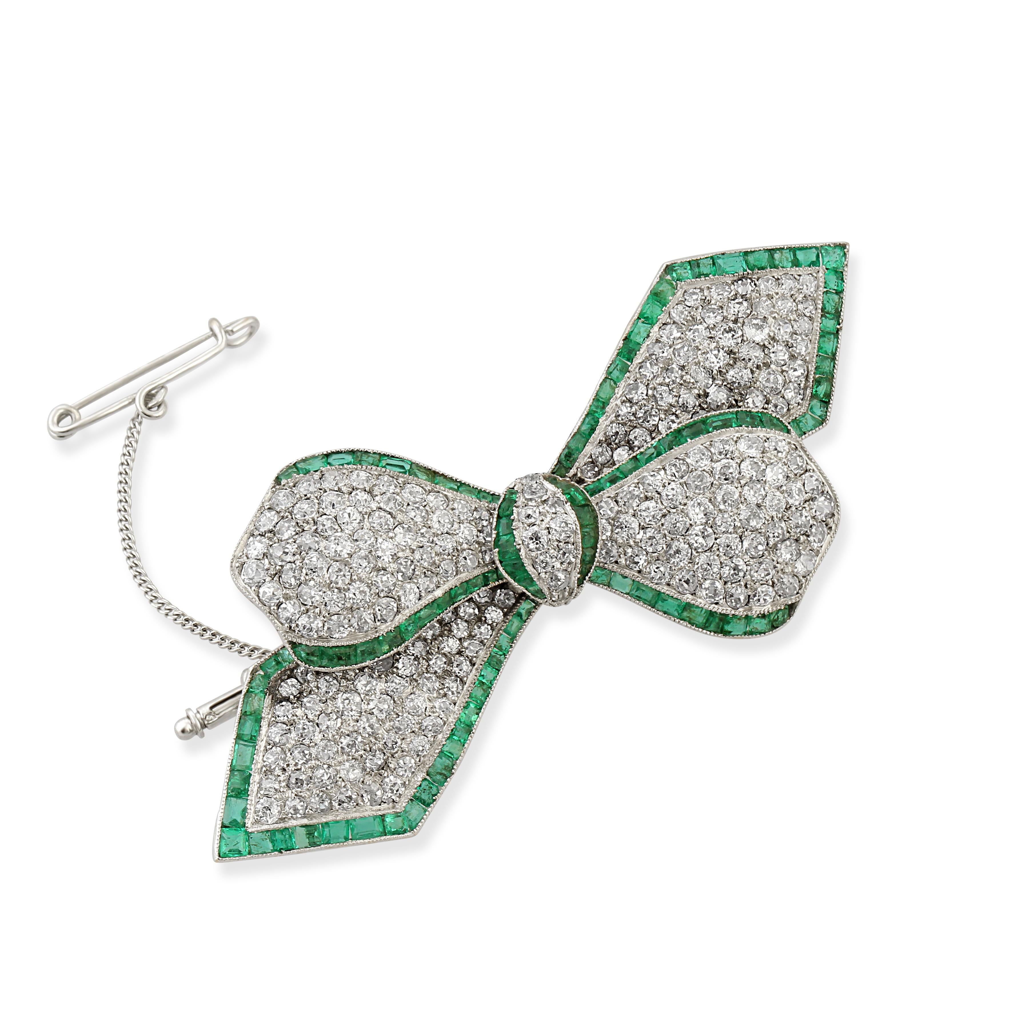 An 18k white gold emerald and diamond bow brooch. Pavé set with diamonds and a rim of calibre-cut emeralds.
