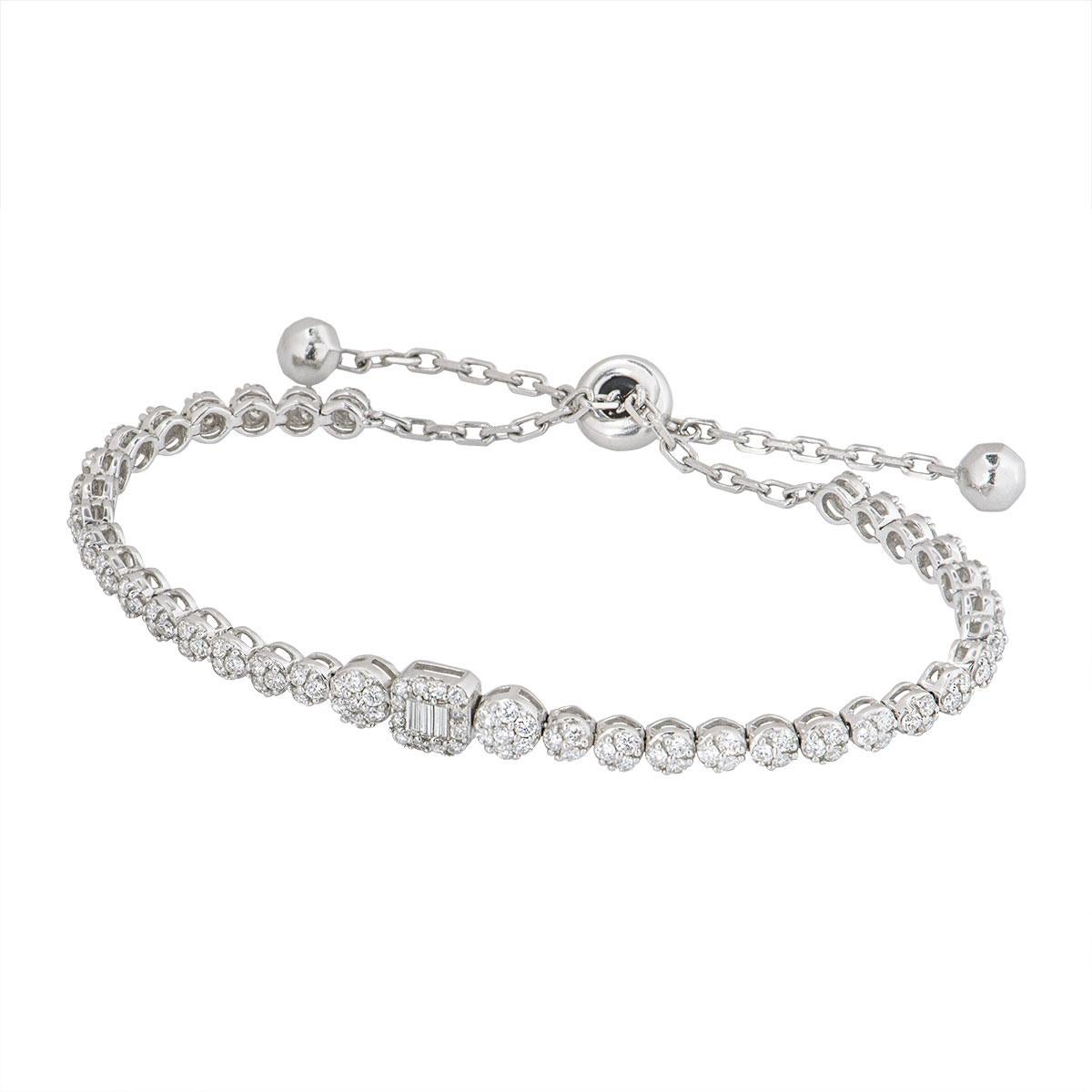 An 18k white gold illusion set diamond line bracelet. The bracelet is set with 128 round brilliant cut diamonds in circular motifs with 3 baguette diamonds in the centre motif. The round brilliant cut diamonds have an approximate weight of 0.77ct