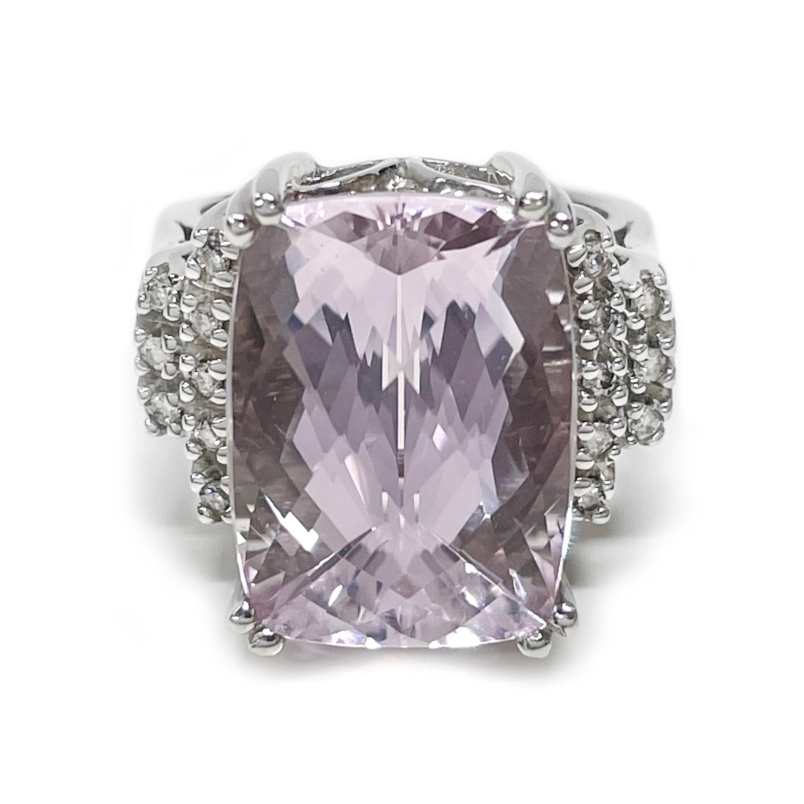 14 Karat White Gold Kunzite Diamond Cocktail Ring. The ring features a large cushion/checkboard-cut Kunzite, 13.8 carat gemstone prong-set on a raised gallery. Eight round side diamonds adorn either side. The wide band slightly tapers. The ring size