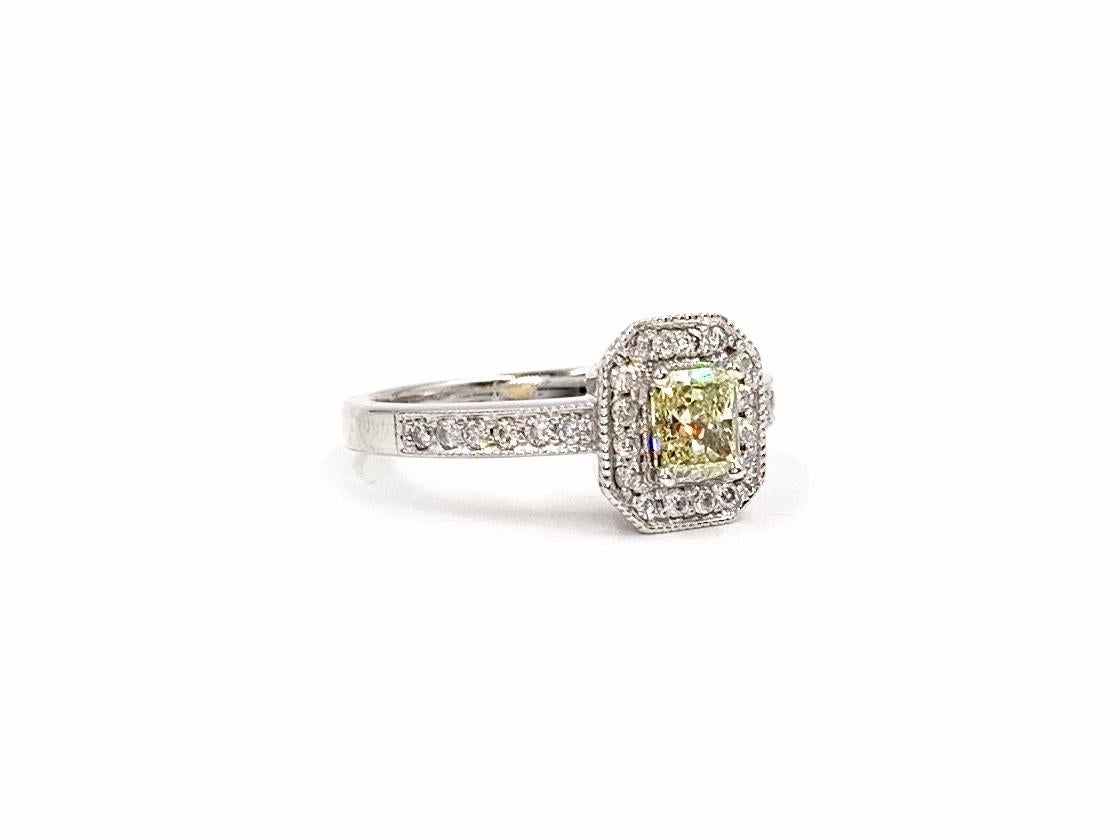 A beautiful 14 karat white gold ring featuring a stunning radiant cut light yellow diamond weighing approximately .65 carats surrounded by a halo of white diamonds and milgrain detail. Radiant diamond has eye clean clarity and generous amount of