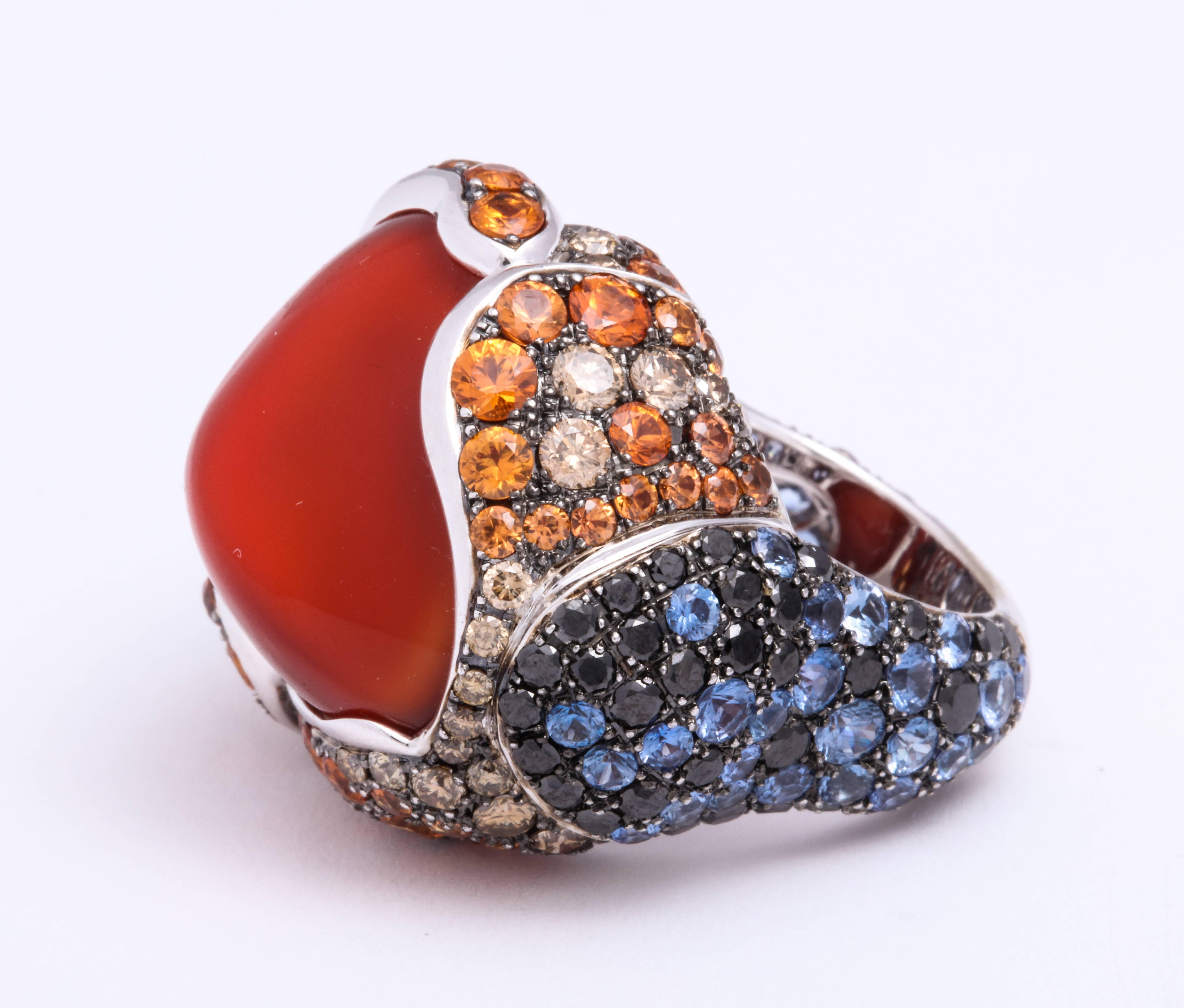 Stylish Ethiopian free-form red opal: 24.38 carats, bezel-set in bohemian chic 18 Karat white gold dome ring decorated with pave'-set round diamond-cut orange sapphires: 3.81 carats, blue sapphires: 3.05 carats, chocolate diamonds: 1.09 carats and