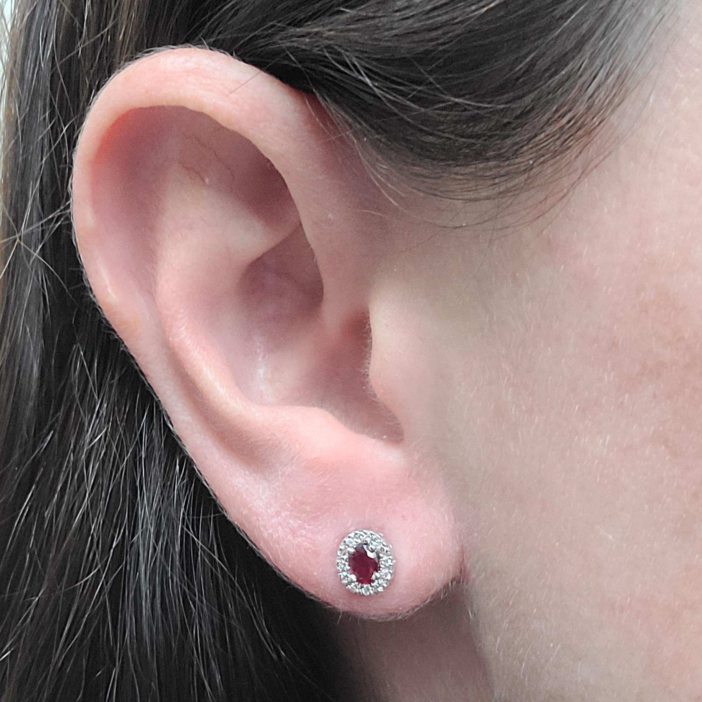 14 Karat White Gold Stud Earrings Featuring 2 Oval Cut Rubies Totaling 0.34 Carats Surrounded By 24 Round Brilliant Cut Diamonds Of VS Clarity & G/H Color Totaling 0.12 Carats.