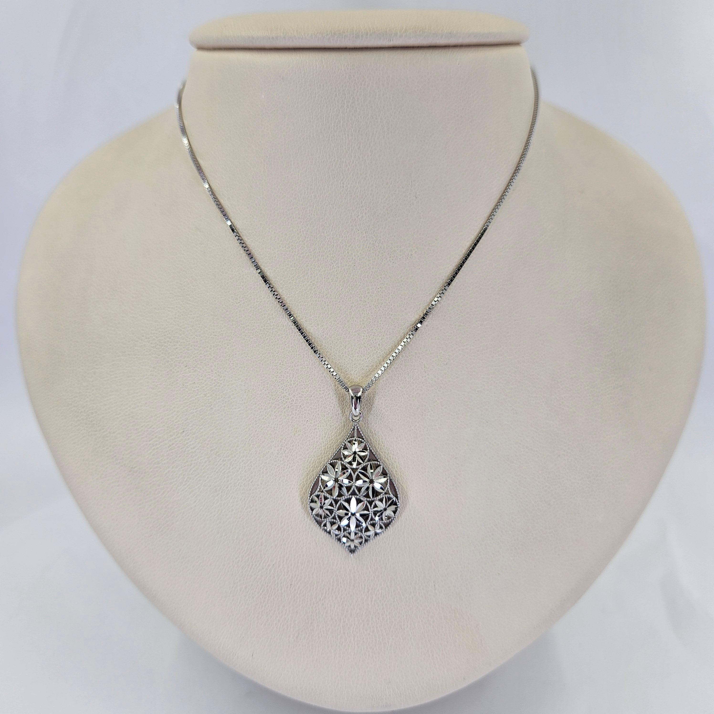 Collana in oro bianco 14 carati con ciondolo a goccia a forma di pera con accenti floreali. Catena a scatola da 18 pollici con chiusura a moschettone. Il peso finito è di 4,6 grammi.

Sono disponibili anche orecchini abbinati.