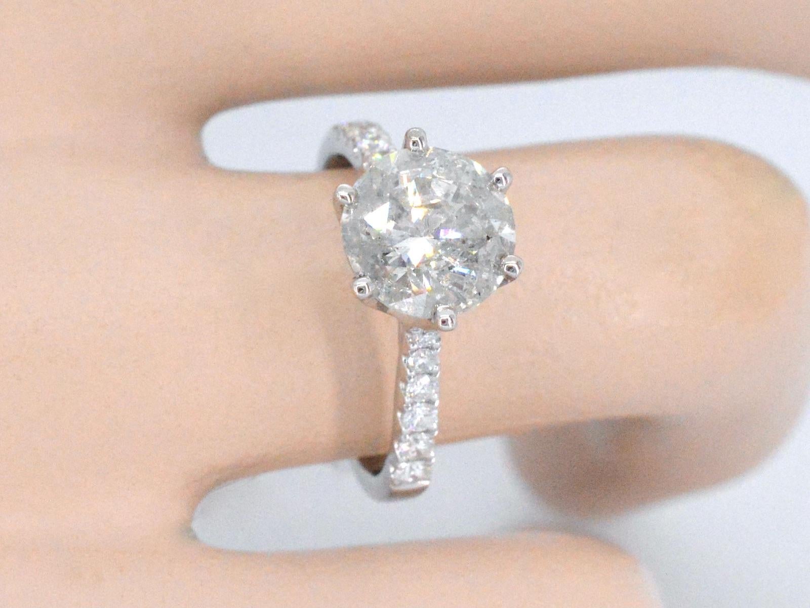 This is a stunning new diamond ring with a 3.00 carat natural center stone and 12 additional diamonds weighing a total of 0.50 carats. The center stone is of excellent quality, with a brilliant cut, D-E color, and P clarity, and the 12 smaller
