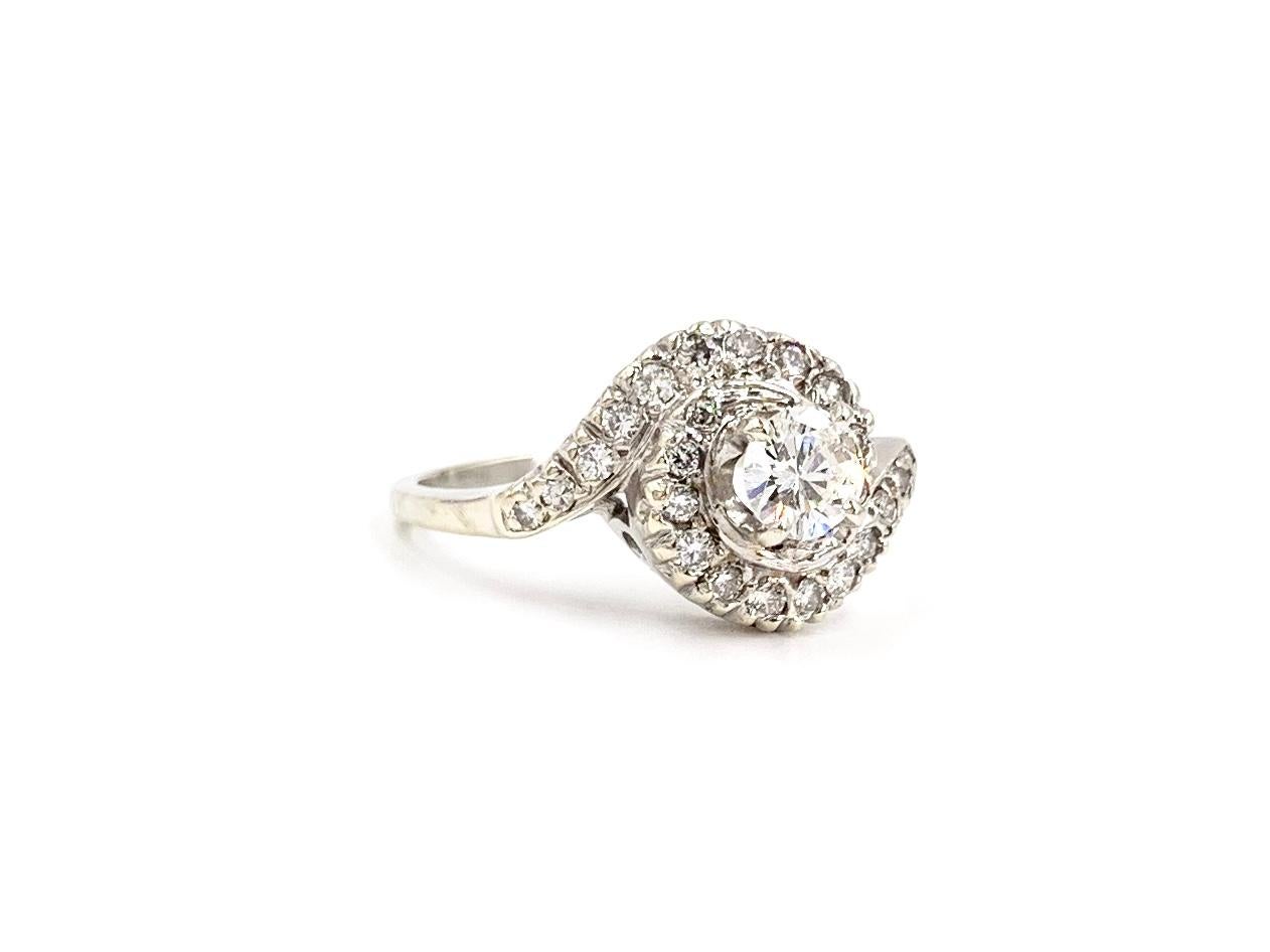 Circa 1960's, a 14 karat white gold elegant vintage swirl diamond engagement ring that can certainly be worn as a fashionable right hand ring. This beautiful piece features a .40 carat round brilliant center surrounded by 24 diamonds at