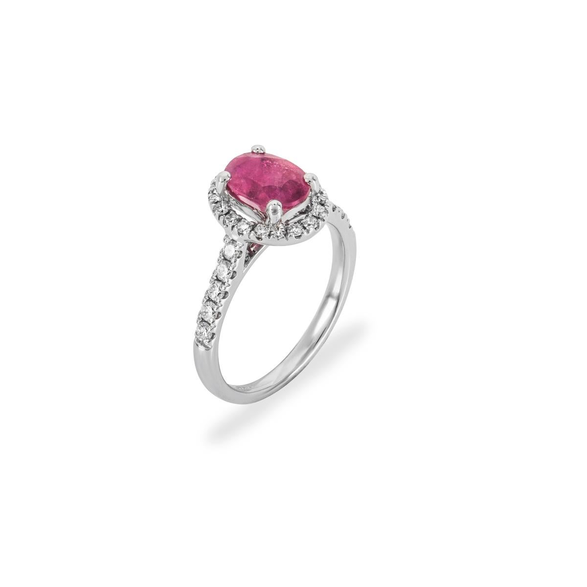 A beautiful 18k white gold ruby and diamond halo ring. The ring is set to the centre with an oval cut ruby weighing approximately 1.28ct, with a milky red hue throughout. Further complementing the ruby are 28 round brilliant cut diamonds pave set to