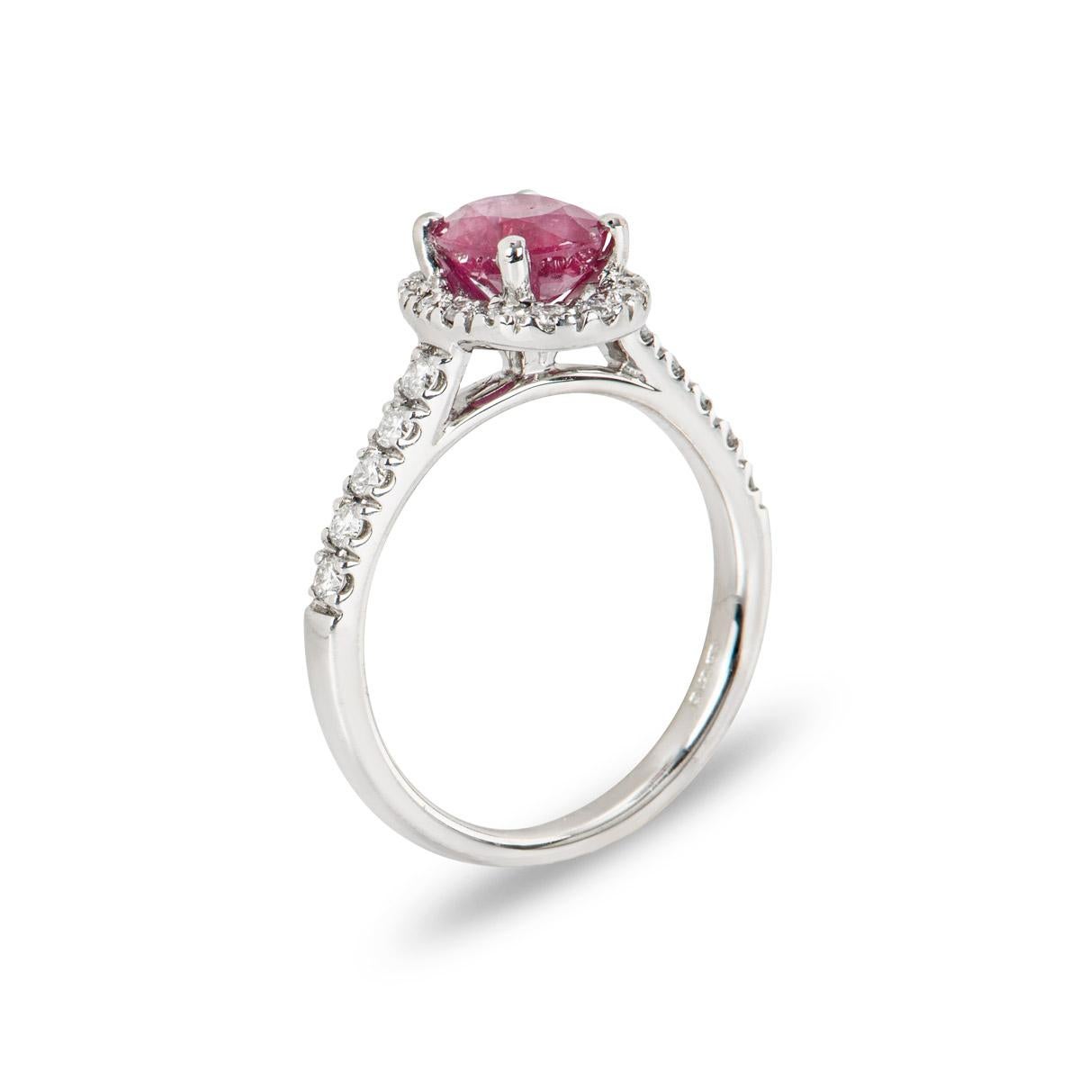 A beautiful 18k white gold ruby and diamond halo ring. The ring is set to the centre with an oval cut ruby weighing 1.53ct, displaying a medium red hue. Accentuating the ruby are 24 round brilliant cut diamonds adorning the halo and shoulders with