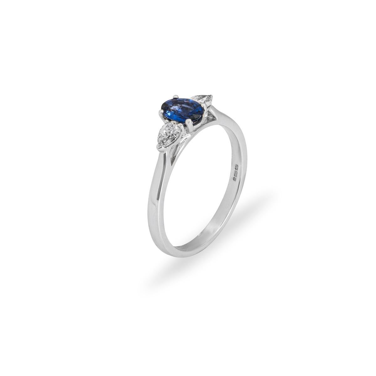 An 18k white gold sapphire and diamond ring. The ring is set to the centre with an oval cut sapphire weighing 0.26ct, displaying a rich even tone. Either side of the central stone sit single pear cut diamonds each weighing approximately 0.16ct,