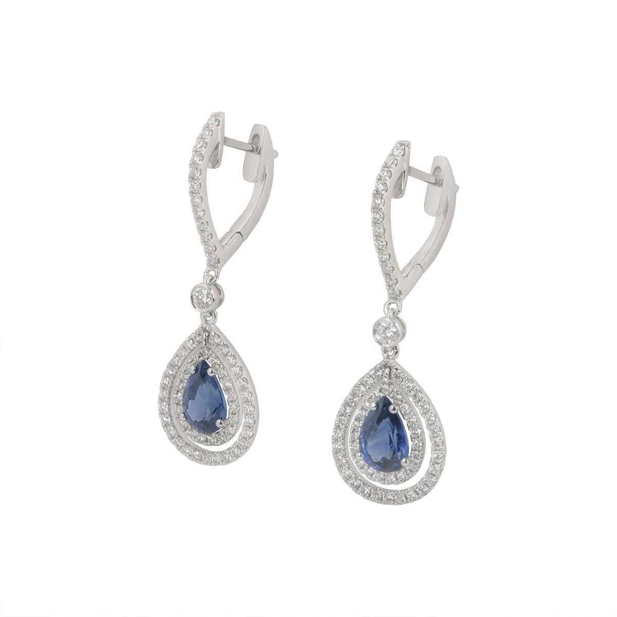 A pair of 18k white gold sapphire and diamond earrings. The earrings feature a pear cut sapphire in a prong setting with 118 pave set round brilliant cut diamonds around it. The pear cut sapphires have a total weight of 1.63ct and the pave set