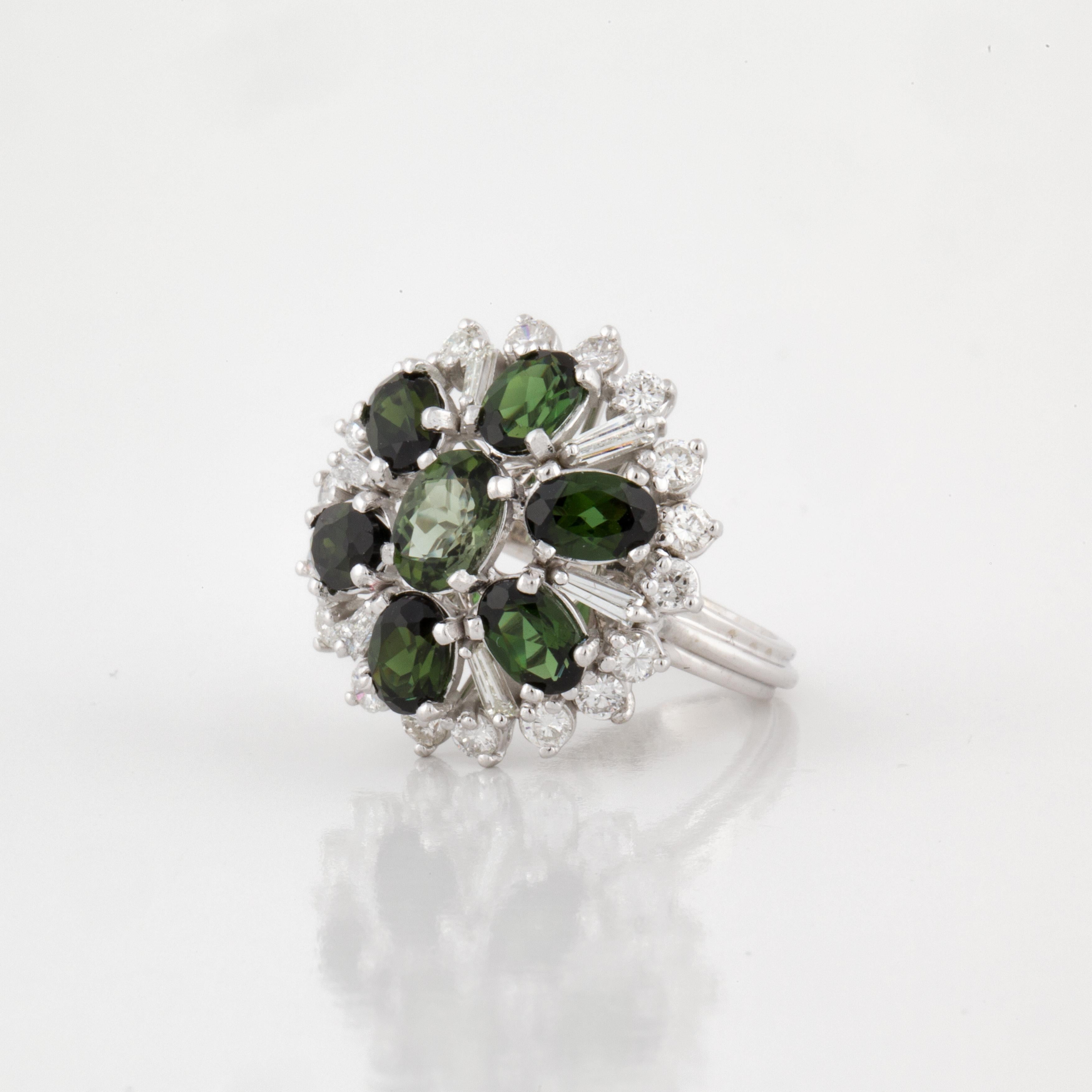 14K white gold cluster ring featuring oval cut green tourmalines accented by round and tapered baguette diamonds.  The diamonds total 1.50 carats; G-I color and VS1-SI1 clarity.  Ring is currently a size 6.  Measures 7/8 inches across and stands 3/8