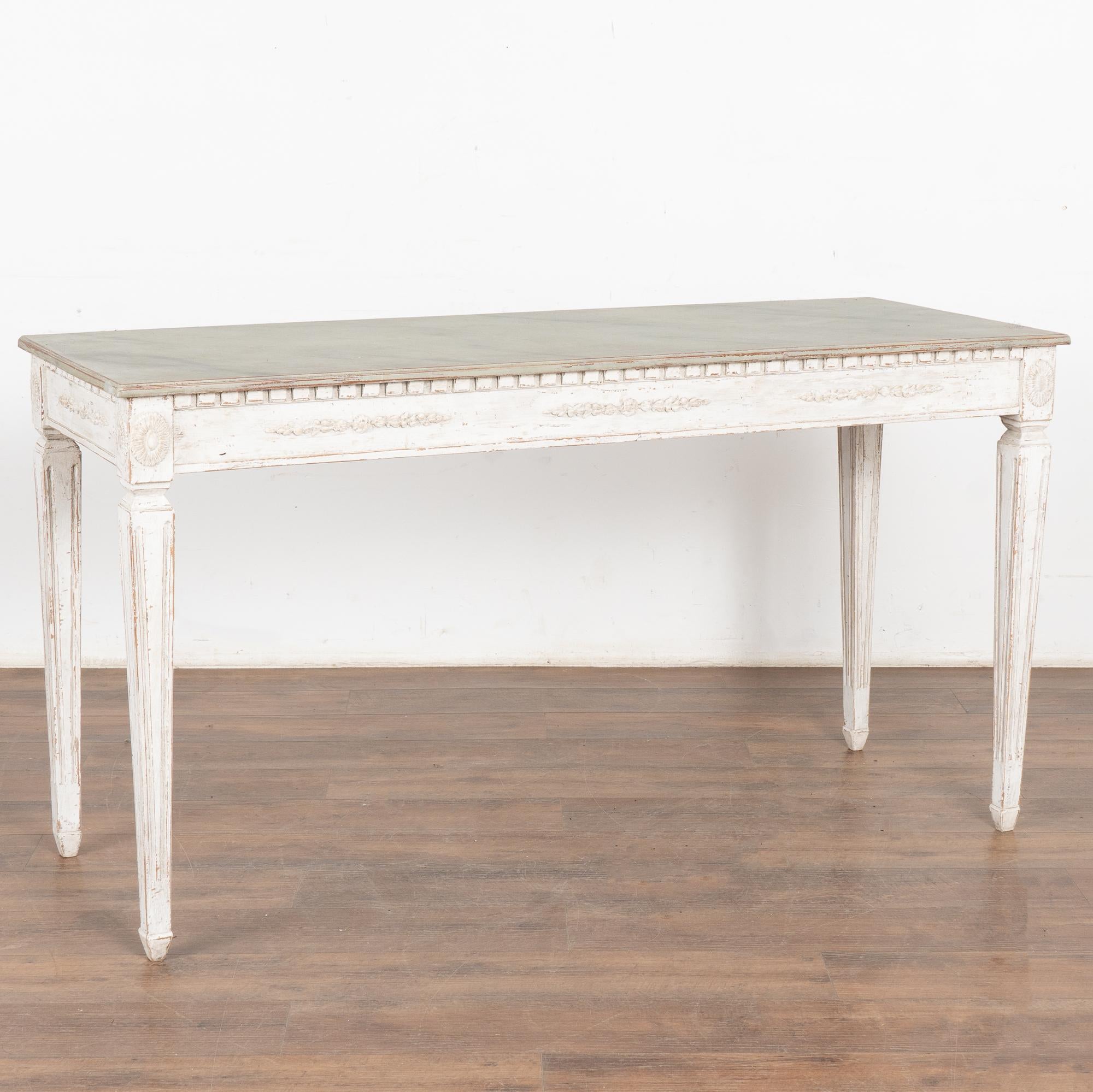 Elegant Gustavian style console table with dentil molding, delicate applied carving along skirt and raised on tapered fluted legs.
It is the stunning, later applied professional painted finish in layers of white and contrasting faux marble top in