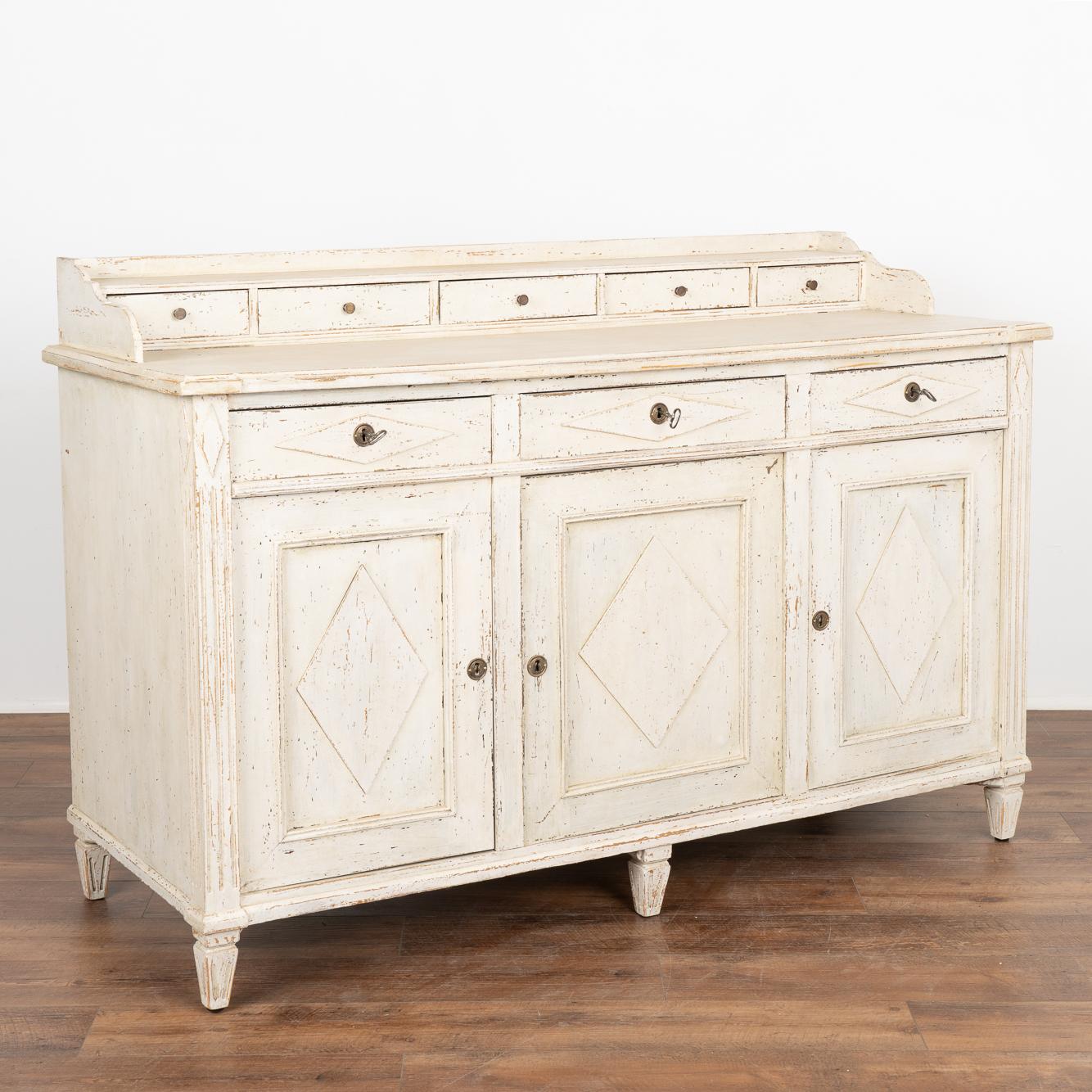 Gustavian white painted pine sideboard or buffet server with traditional decorative Swedish diamond panels along drawers and doors, raised on tapered fluted feet.
Unique to this cabinet is the additional five small drawers above the serving