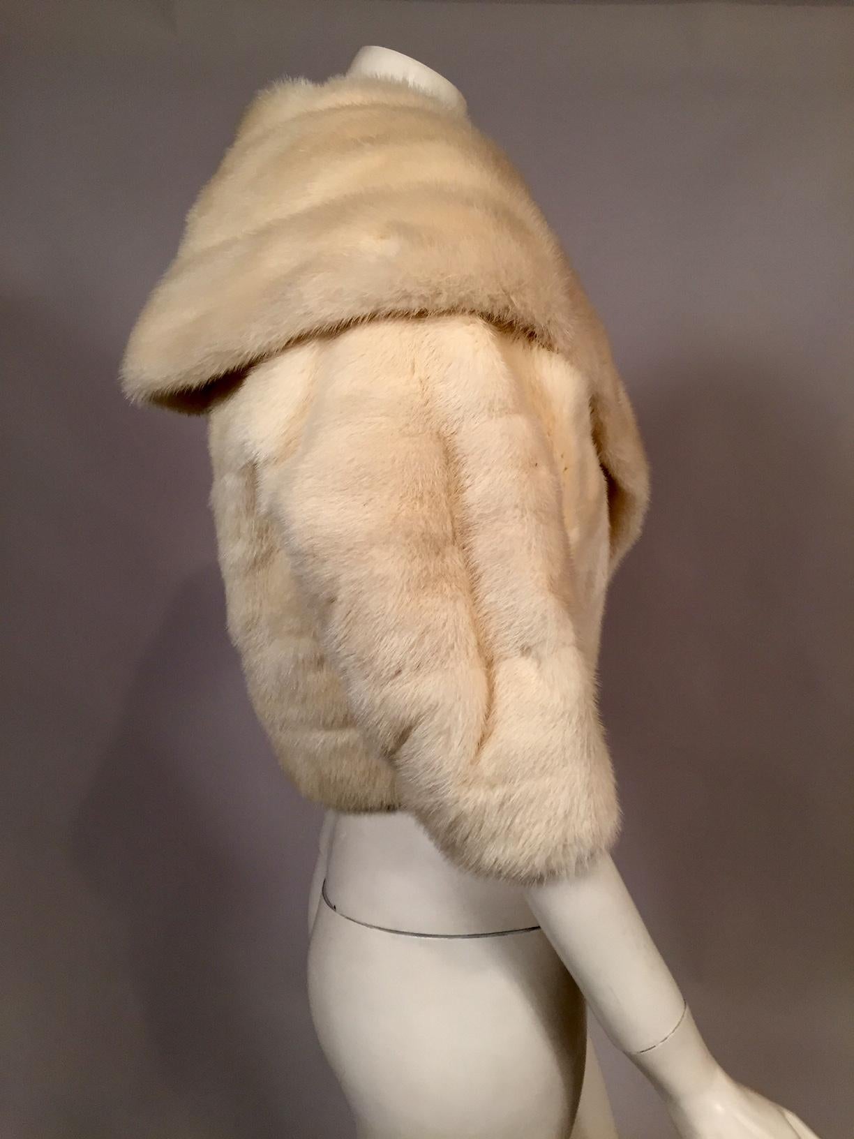 This gorgeous white mink jacket has a generous shawl collar and the pelts are worked horizontally throughout. The jacket closes with a single fur hook at the center front and it is lined with and ivory and gold metallic brocade. There is an interior