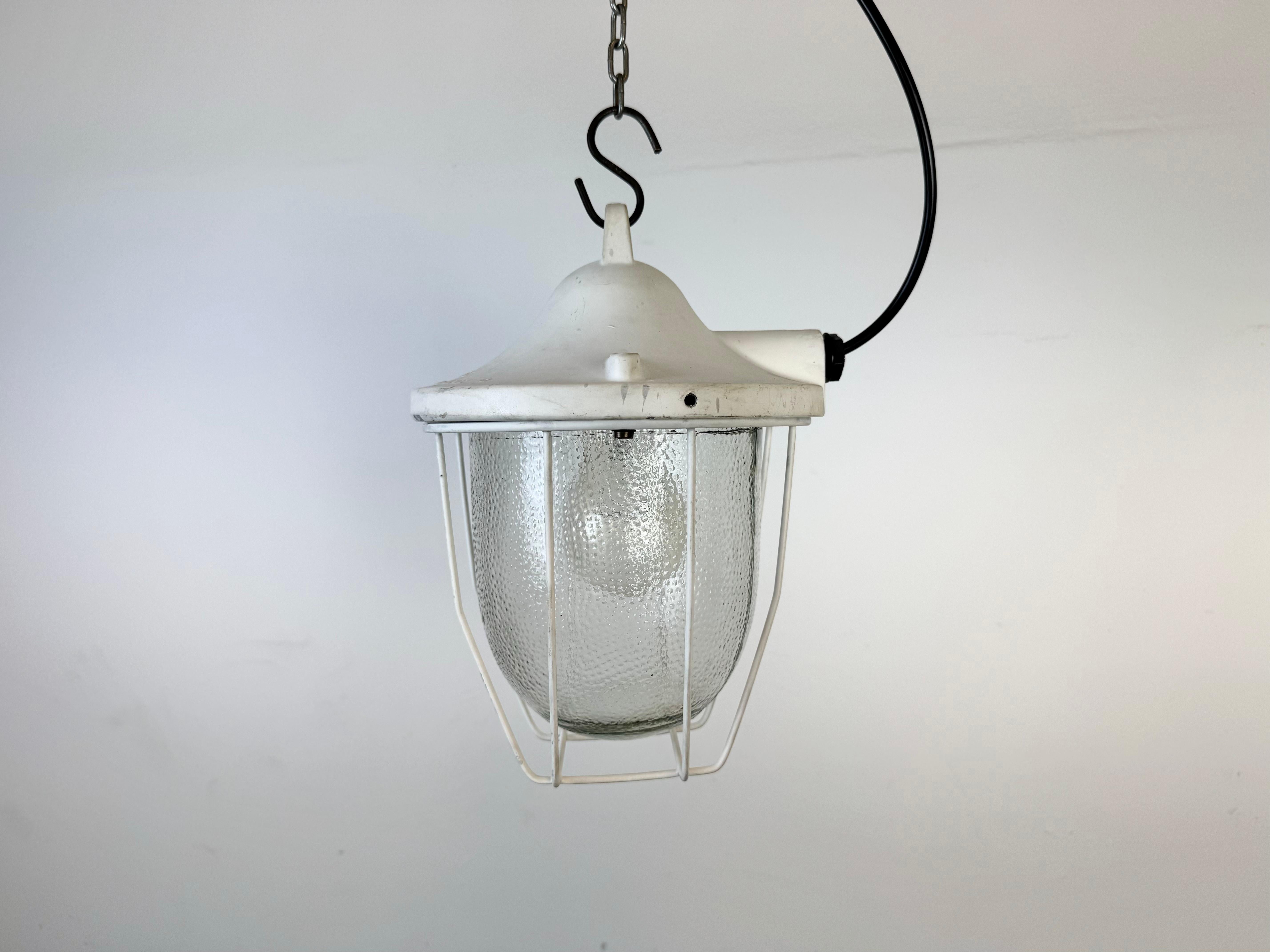 White industrial lamp made by Polam Gdansk in Poland during the 1970s. It features a cast aluminium body, an iron cage and a frosted glass. The porcelain socket requires standard E 27/ E 26 lightbulbs. New wire. The weight of the lamp is 2 kg.