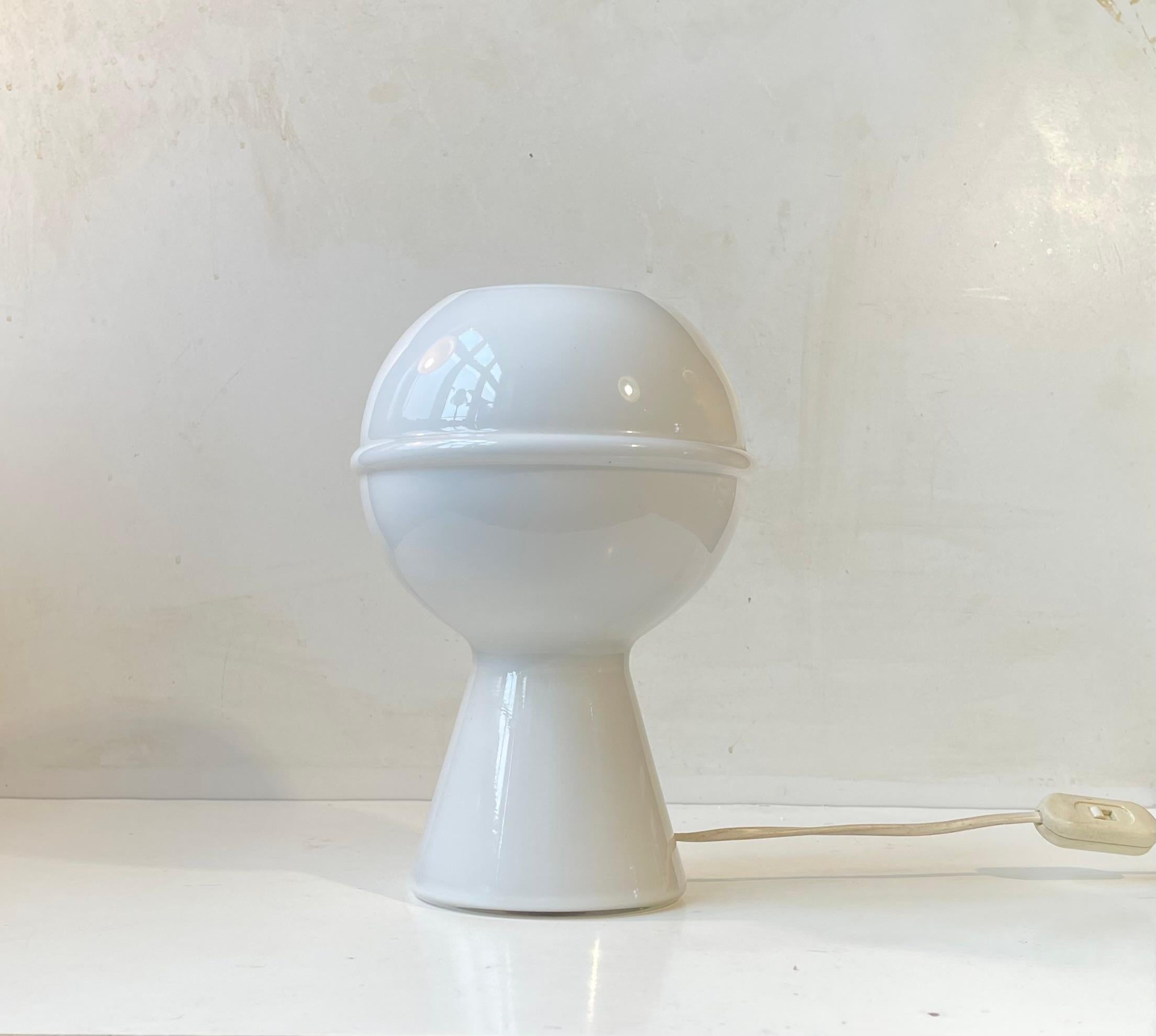 A stylized Saturn table light. Executed in handblown cased white opaline glass. Featuring an on/of switch to its cord. Manufactured in Murano, Italy during the 1970s. Measurements: H: 24 cm, Diameter (shade/base): 17/11 cm.  

For the US. It will