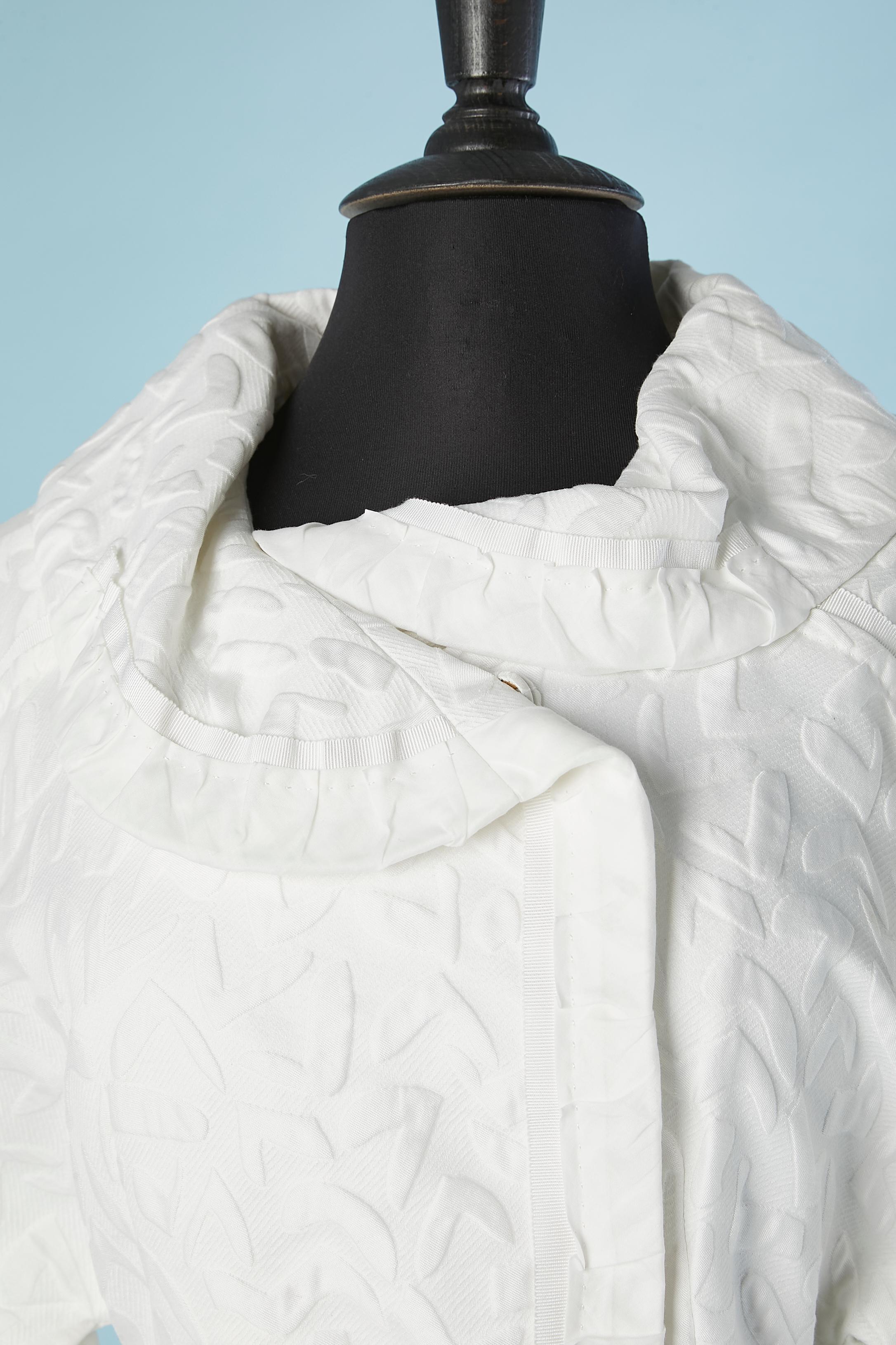 Ensemble manteau et jupe en coton jacquard blanc. Manteau double boutonnage fermé par un bouton pression (recouvert de tissu). Ceinture en gros grain.
Jupe se fermant sur le côté gauche par une fermeture éclair, nœud gros grain au milieu du
