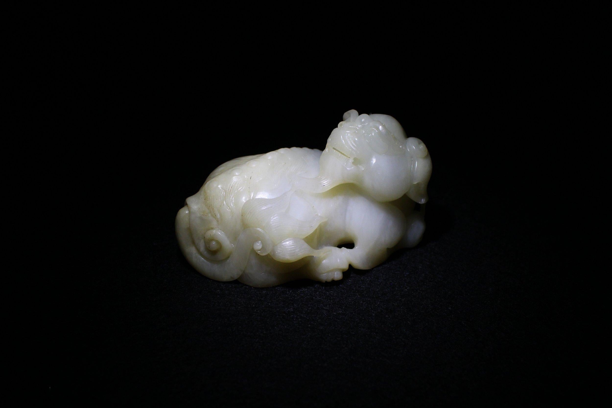 Carved out of white and yellow-toned jade, this beautiful mythical beast rests on its four limbs like a lion in the Serengeti. Each limb is given finely-carved claws and a round pad on the paw. 

On its head, one can see intricately carved teeth,